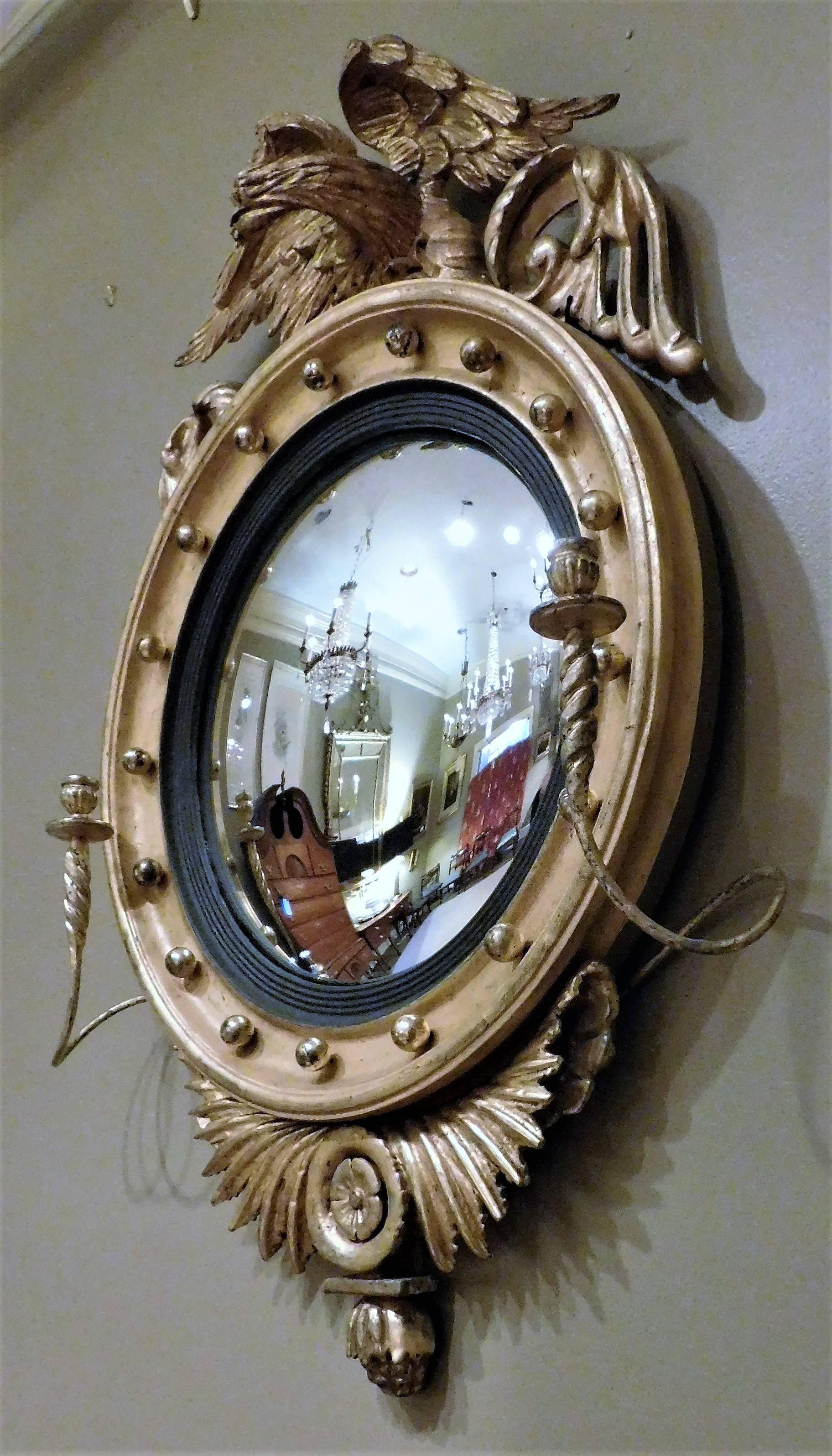 Carved and giltwood convex mirror with candle arms (girandole), featuring spread wing eagle pediment, with ebonized reeded surround, flanked by spiral twist sconces, terminating in carved and gilt wing and rosette. Probably made in New York. This