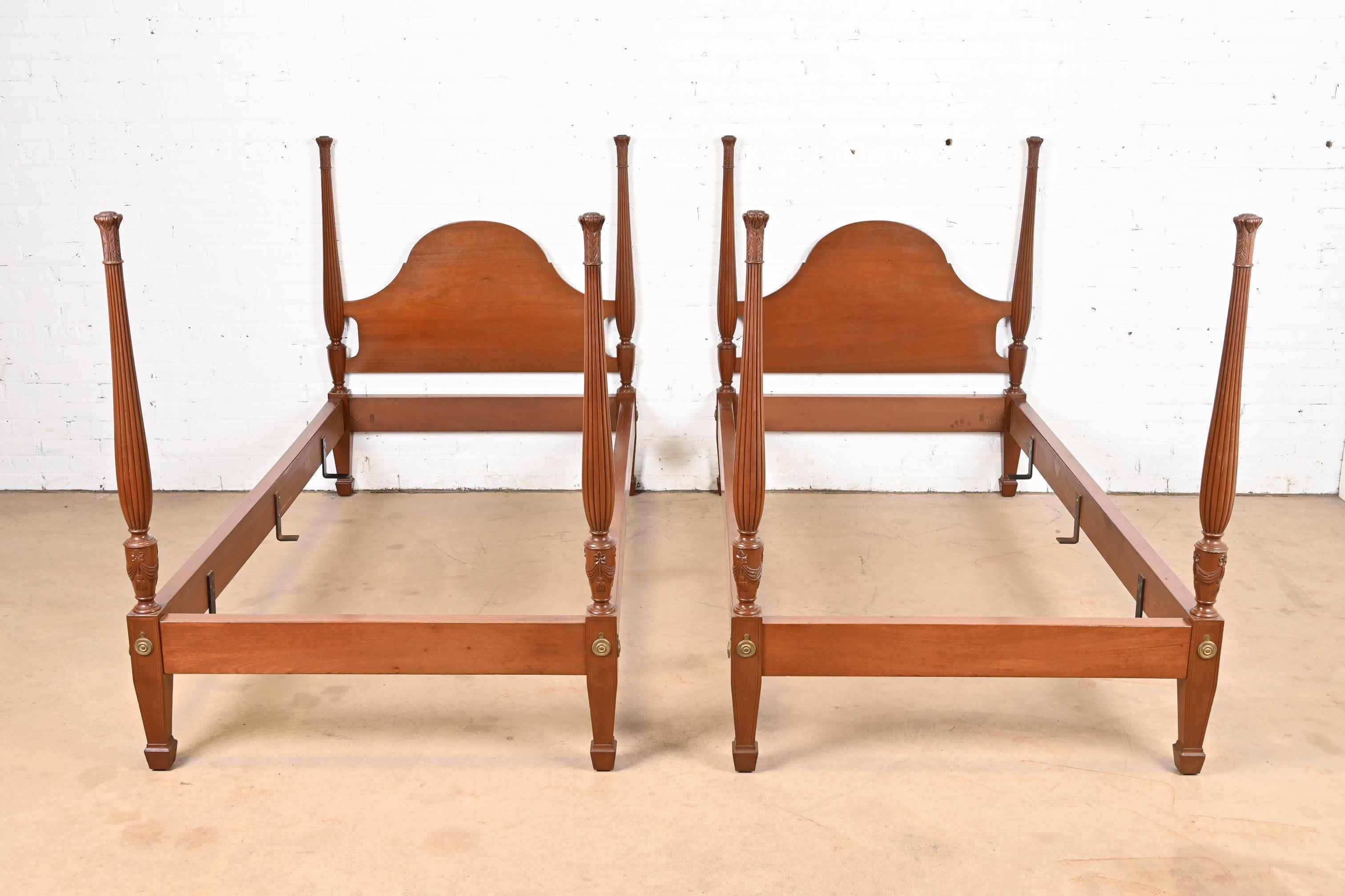 A gorgeous pair of Federal or Georgian style carved mahogany twin poster beds

In the manner of Baker Furniture

USA, Circa Mid-20th Century.

Carved solid mahogany, with brass accents.

Measures: 42.5