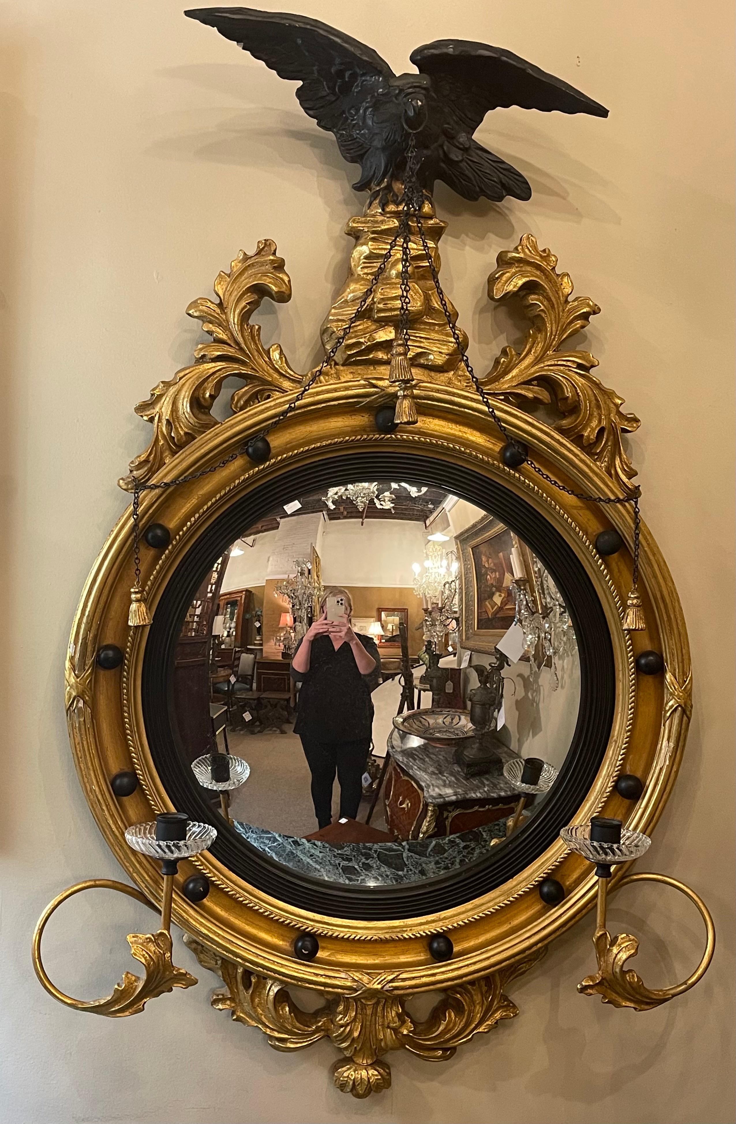 Federal convex bullseye wall mirror, 19th-20th century. A finely carved winged eagle perched above a wonderfully carved wall or console mirror. The candlestick arms having crystal boboches. The whole ebony and gilt gold decorated.