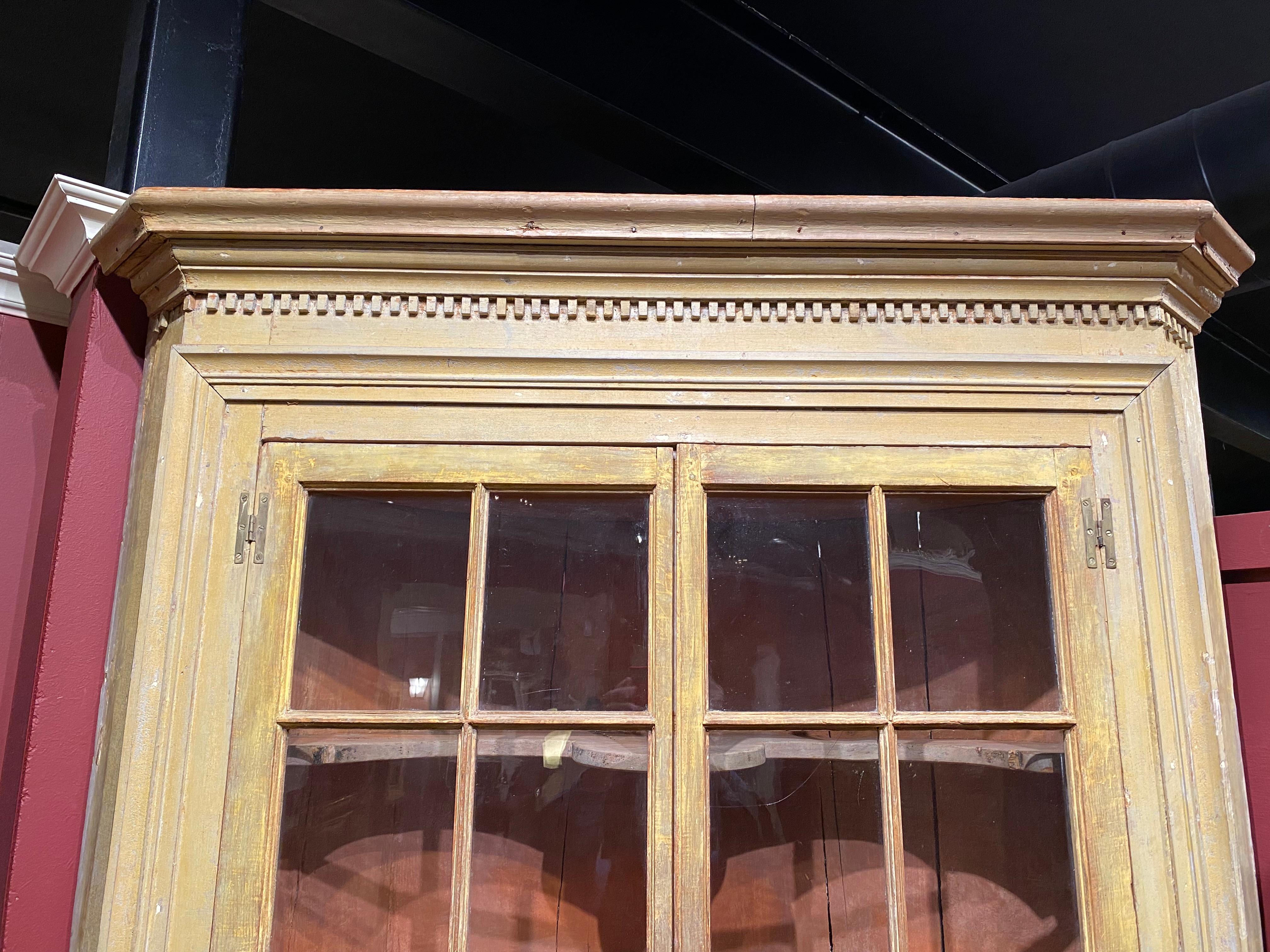 A fine example of a one piece Federal period New England corner cupboard with a barrel back , a molded cornice with dentil molding surmounting two upper case glazed glass multi-panel doors with original wavy panels, opening to a three shaped shelf