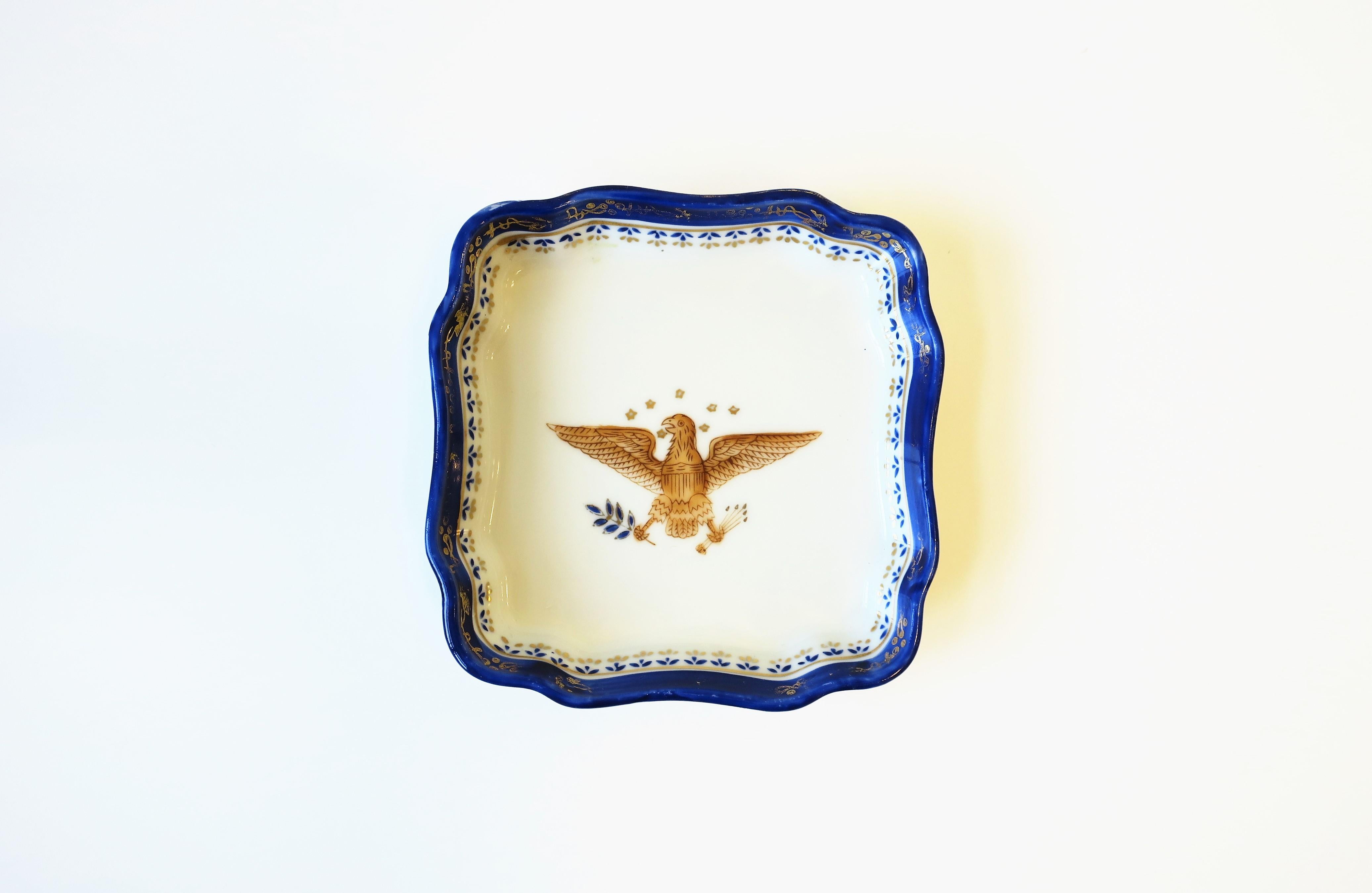 A white porcelain jewelry or trinket dish with blue and gold bird design in the Federal style, circa early to mid-20th century, Europe. A beautiful gold Eagle bird with a halo of stars holding wheat. Great as a standalone piece or to hold jewelry or