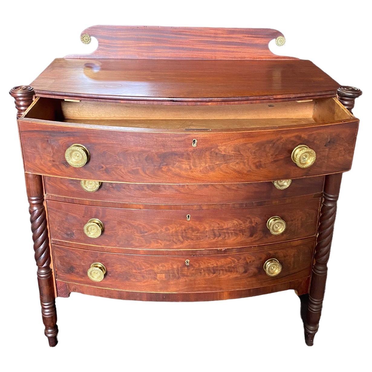 Exceptional early 19th century Sheraton bow front chest of drawers. The case is constructed of lovely flame mahogany. There are four drawers all fitted with the stunningly detailed original brass pulls. The gorgeous flamed top has a nice scroll back