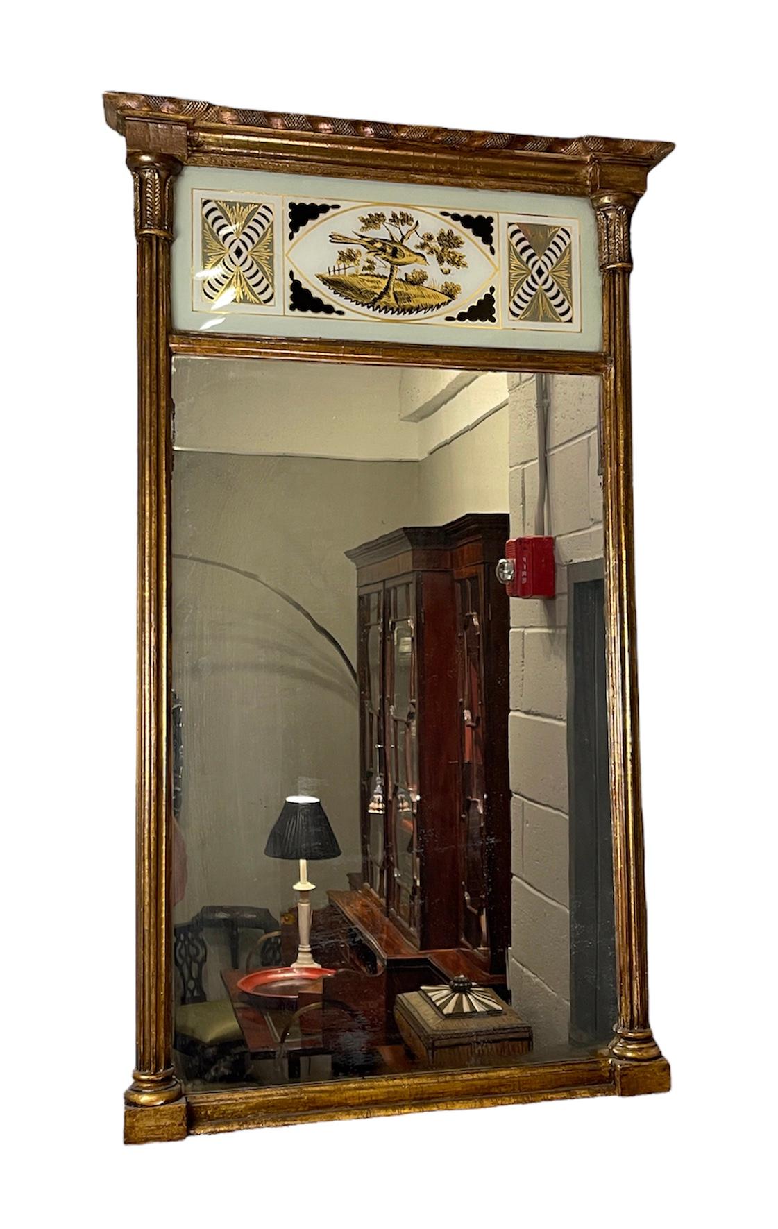 This American Federal gilt-wood mirror dates 
Circa 1790, it’s lower rectangular antique mirror plate below 
A black, white & gold verre eglomise panel. The lower plates flanked by columns having rounded bases and floral capitals. The Top molding