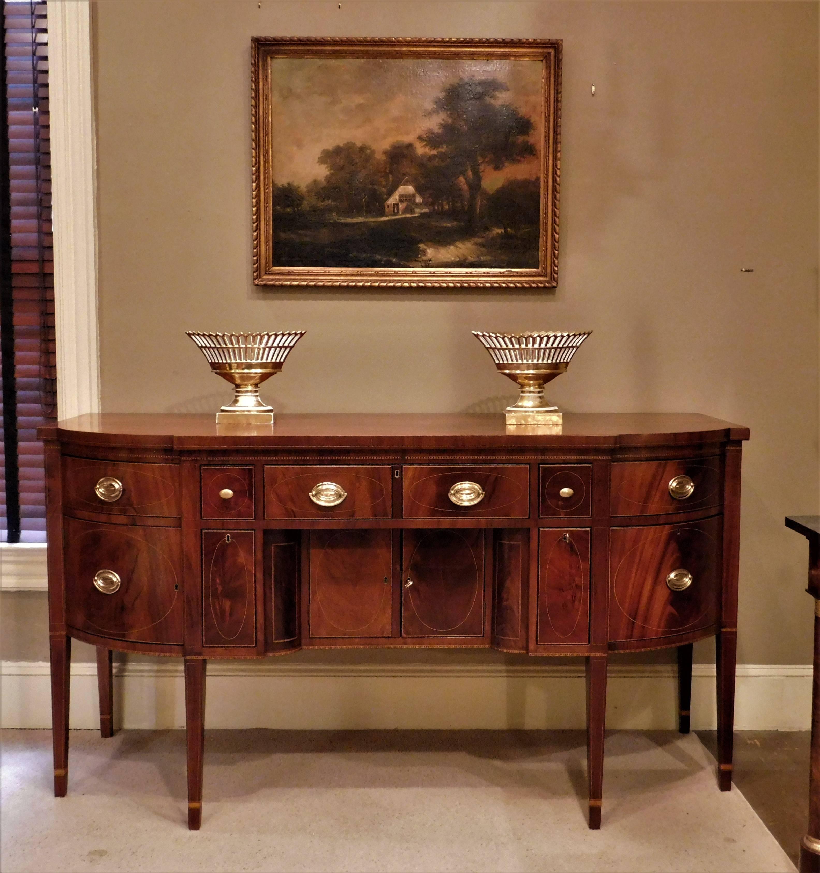 This swell-front Hepplewhite sideboard is mahogany and high figured mahogany with satinwood and ebony inlay and poplar and pine secondary woods. The distinctive and unusual inlay designs included barber pole, arrow, diamond patterns and string. The