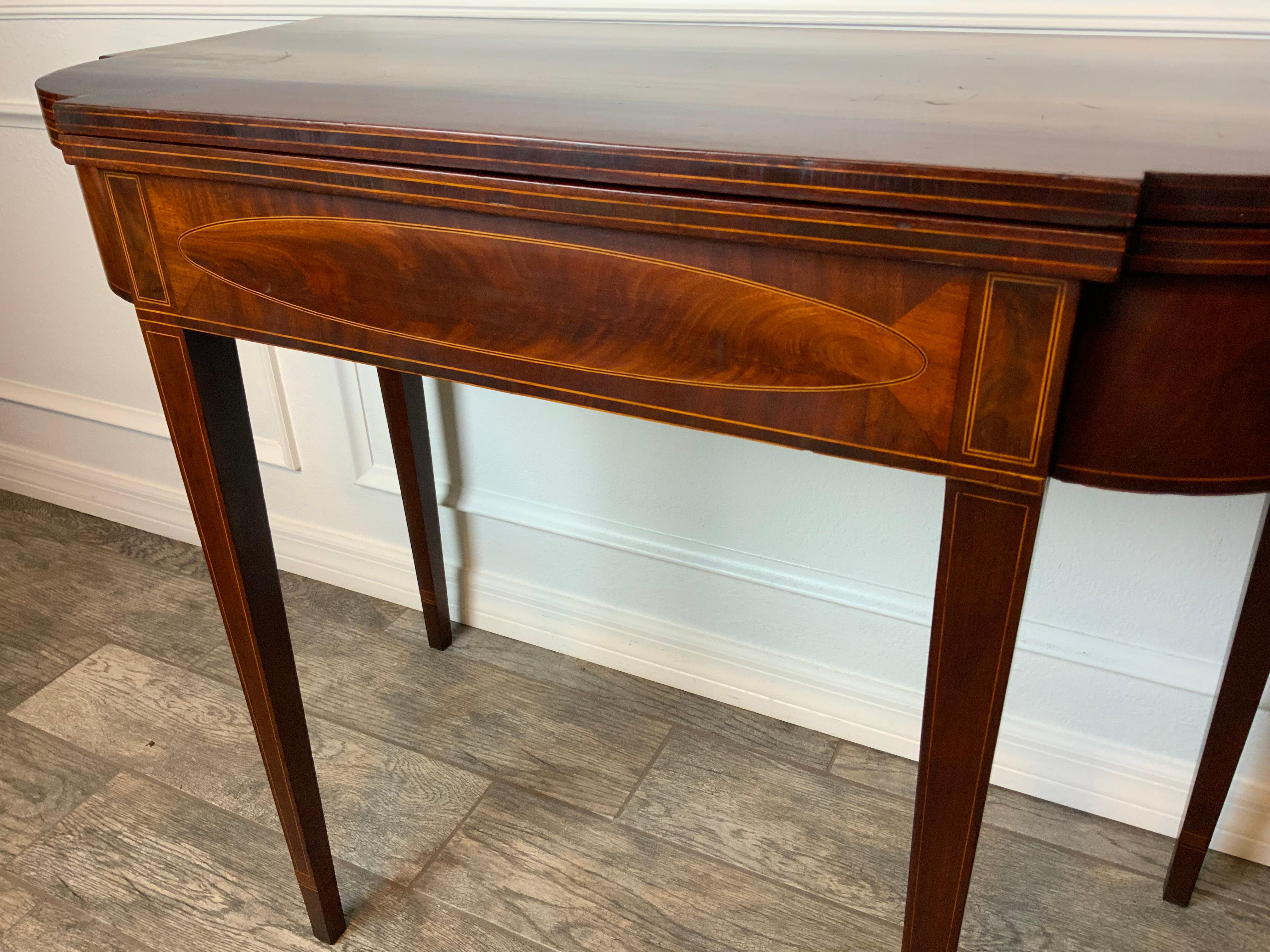 American mahogany inlaid Hepplewhite fold top card table Circa 1790-1800. Tapered straight legs terminating at the feet in simple cuff inlay. Shaped skirt and conforming ovolo shaped corner tops with double string inlay. White Pine and Ash secondary