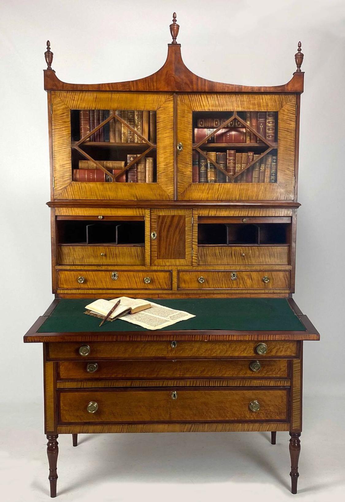 All original in in excellent condition dating to circa 1815. Three part, top section has shaped crest with three turned urn finials above pair of glazed doors; mid-section has centered cupboard fitted with drawers, flanked by tambour doors, interior