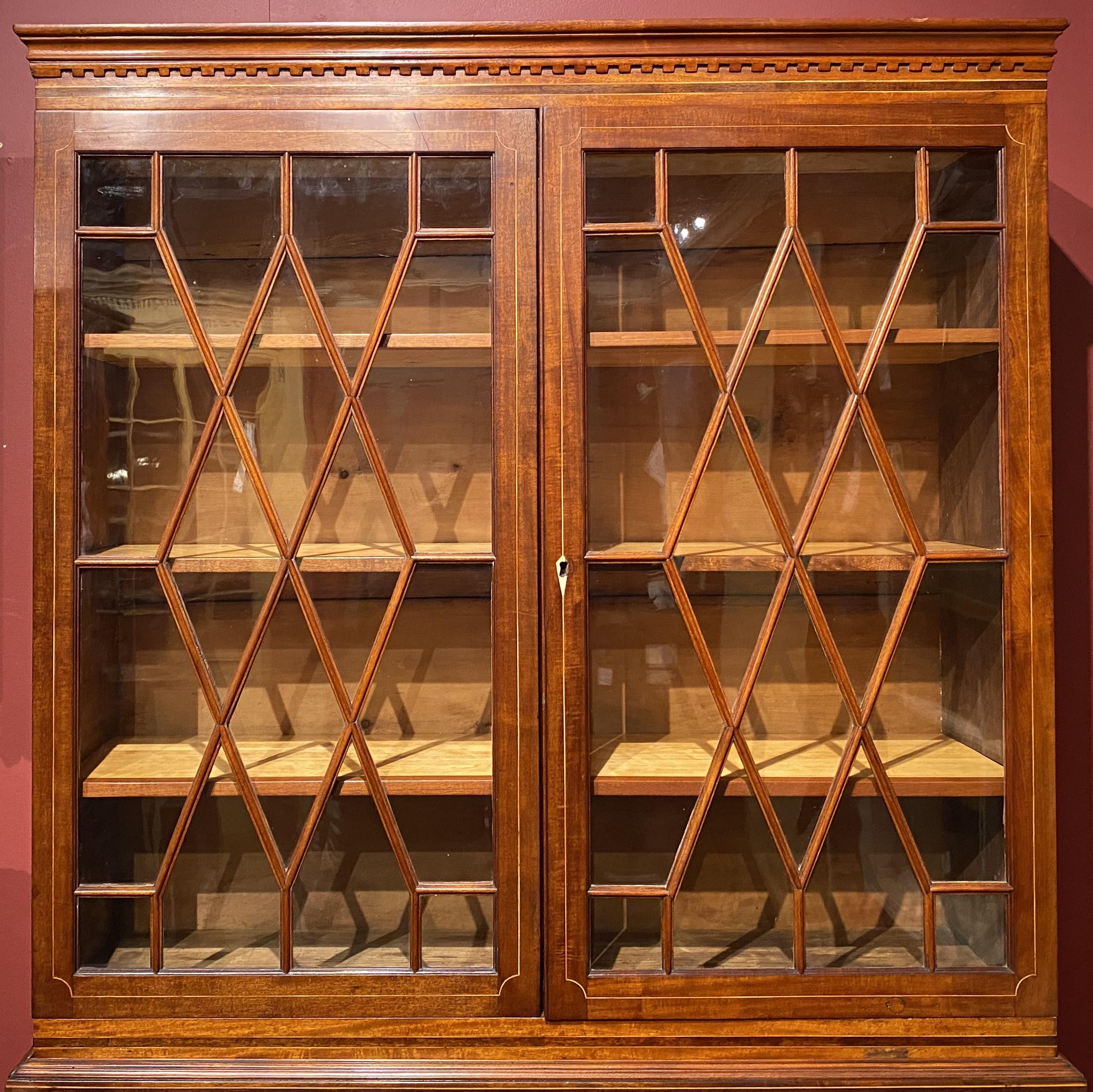 A fine example of a Federal mahogany two part secretary desk, with a dentil molded cornice surmounting an upper bookcase with two 16 pane glazed glass doors with satinwood line inlay, opening to three interior shelves, over a lower case with a