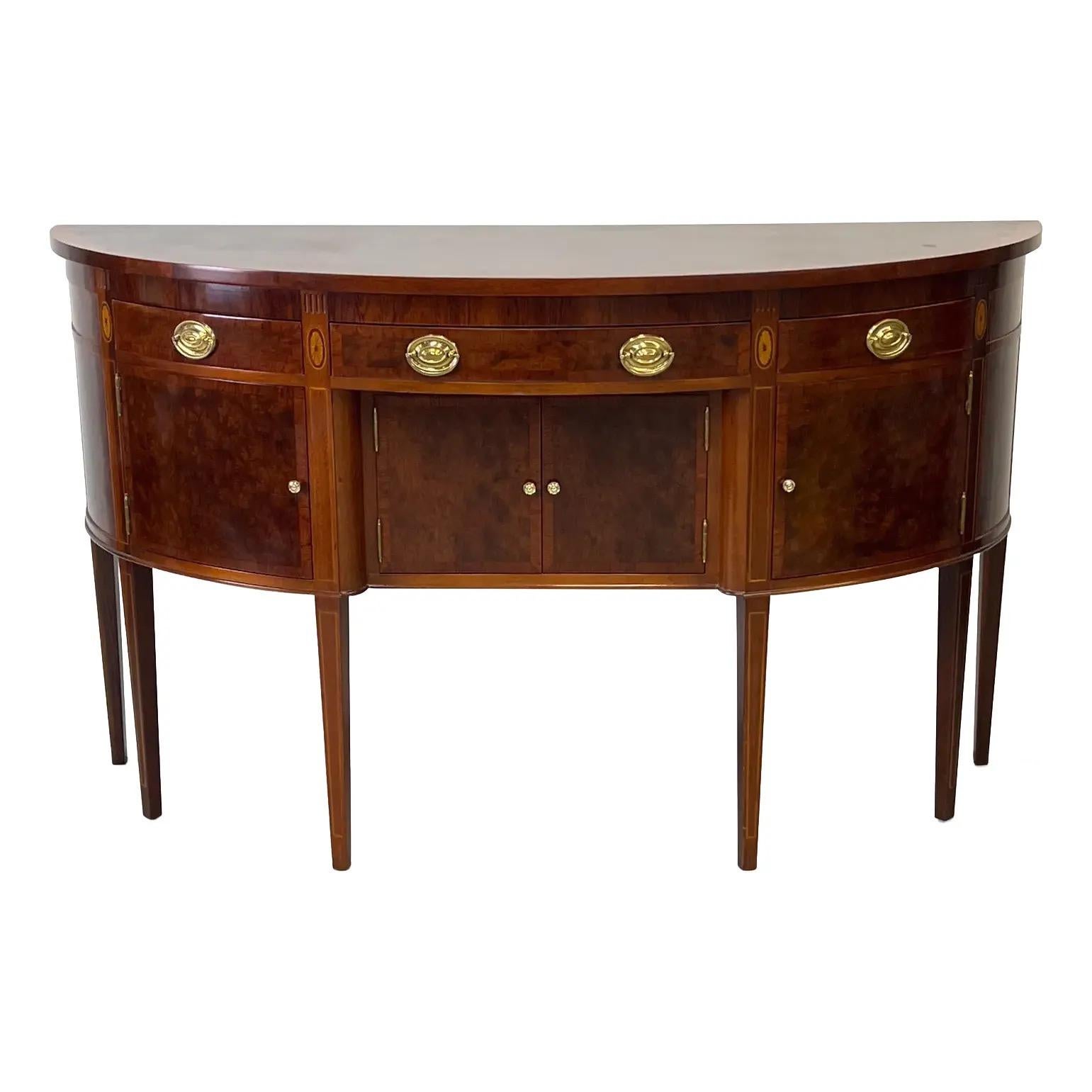 Federal-style mahogany sideboard features a gently bowed front and finely banded veneer work, showcasing craftsmanship from a classic American furniture tradition. It stands on tapered legs and retains its original solid brass oval drawer pulls and
