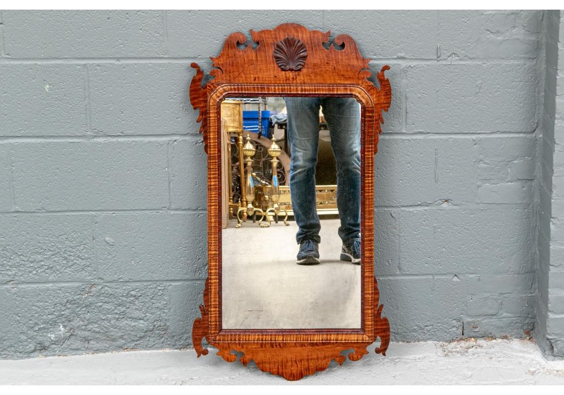 An artisan Federal style carved mirror with mixed woods. Monogrammed RE on the back. 
The outer frame in mahogany with the classic shaped wide crest, ears top and bottom, and wide terminal. The middle surround in a figured wood, the shaped inner