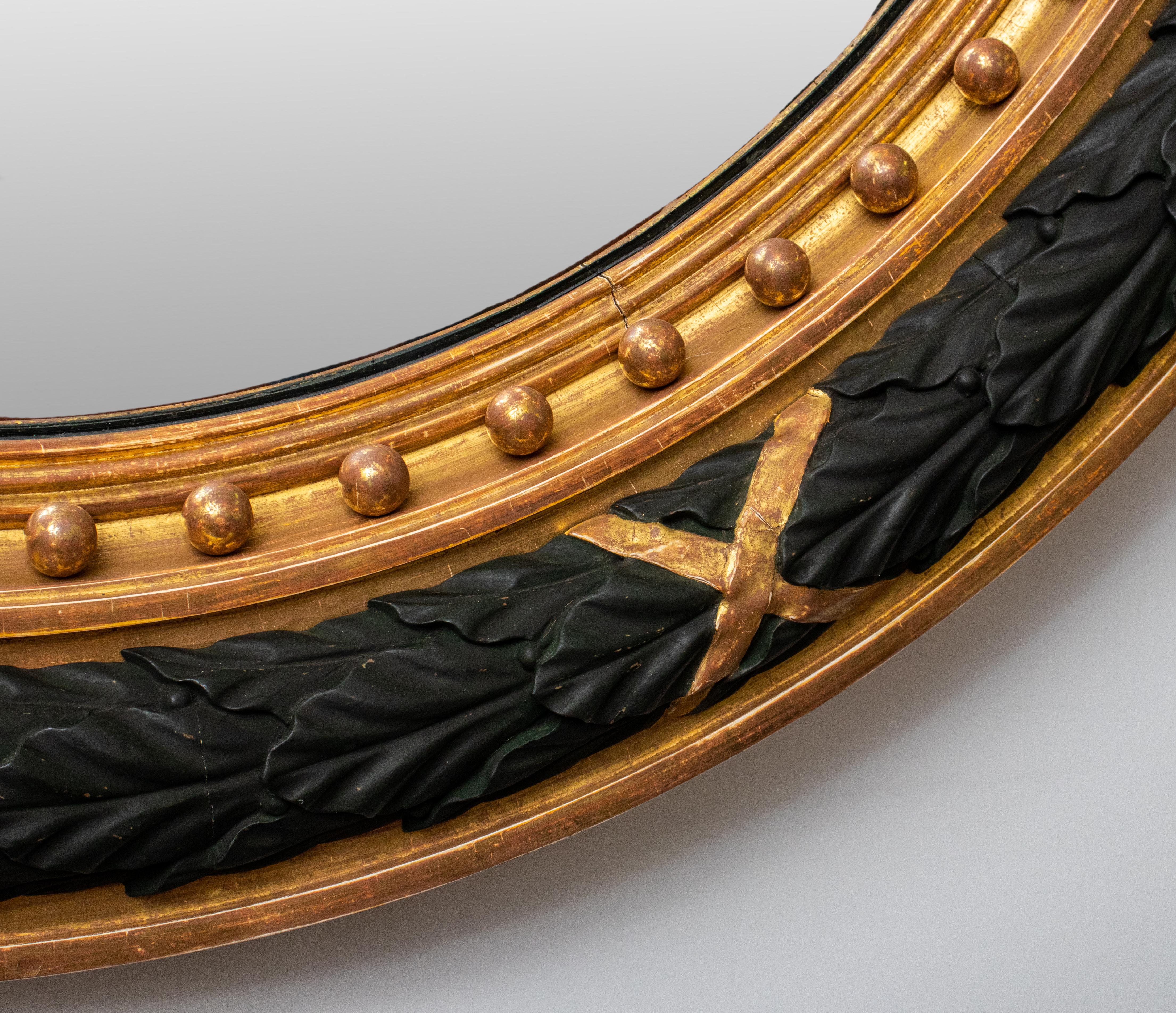 Federal style convex mirror, giltwood and black lacquer, with a laurel wreath border. 
Measures: 38.5 diameter x 4.5 depth.