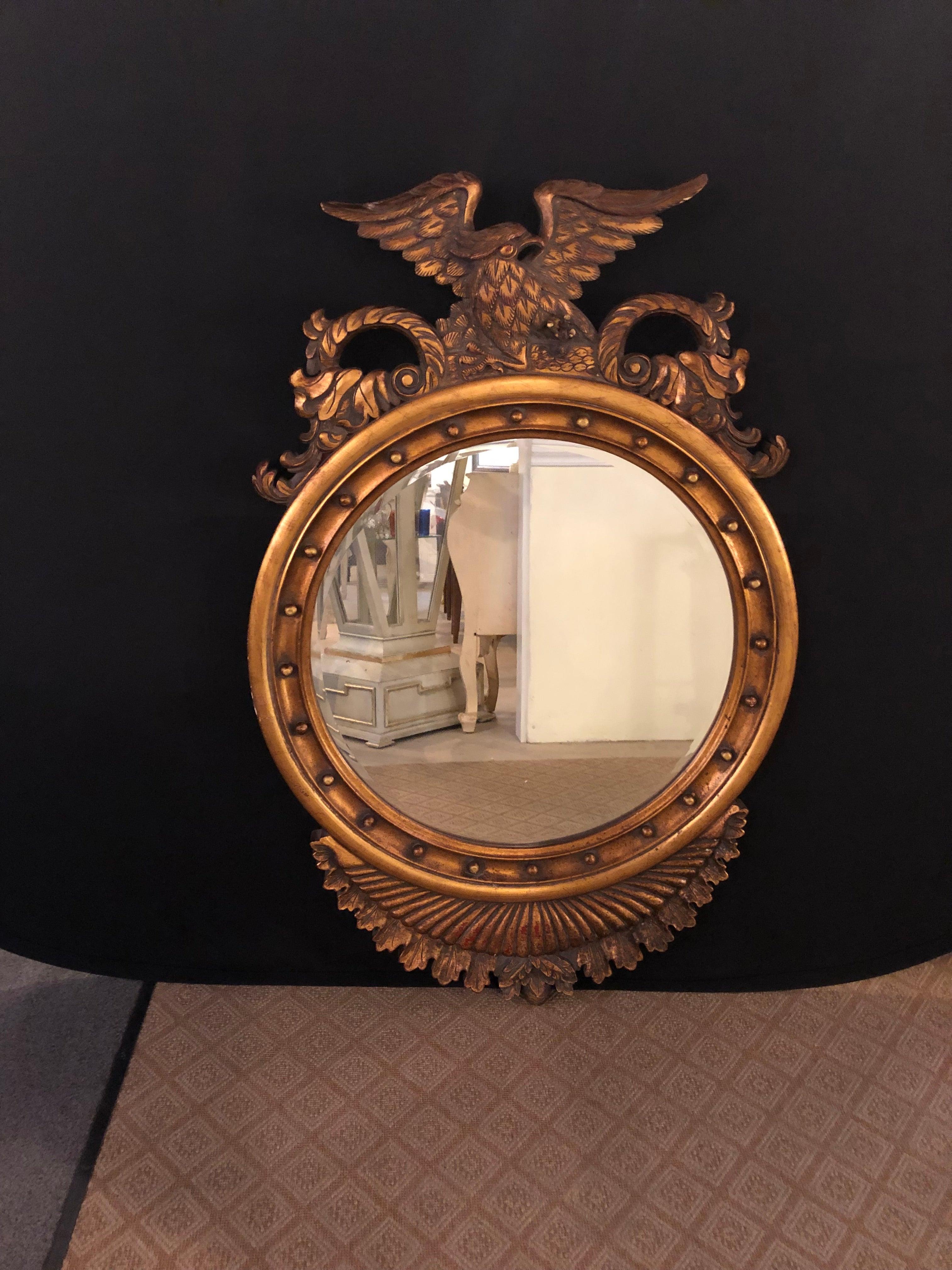 Federal style eagle crested circular wall or console mirror. The finely carved winged eagle over a circular frame in gilt wood decorated with balls around the clear mirror center. The bottom with feather carvings.