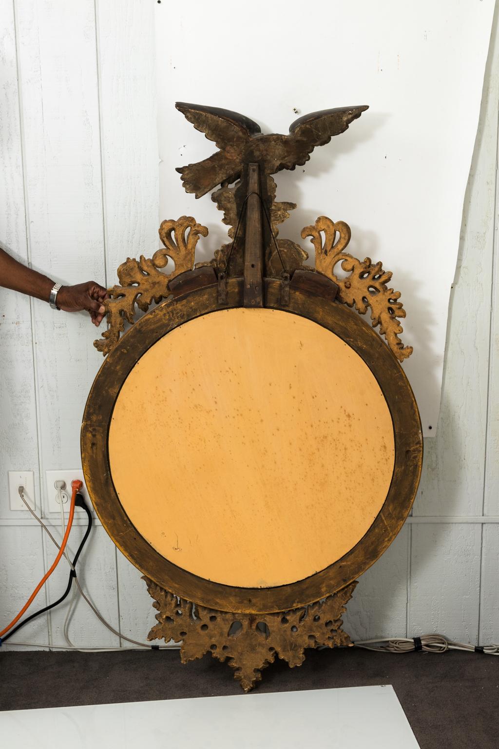 Federal style fish eye convex mirror in giltwood with a heavily carved foliaged crown featuring a black painted eagle, circa late 19th century.
       
