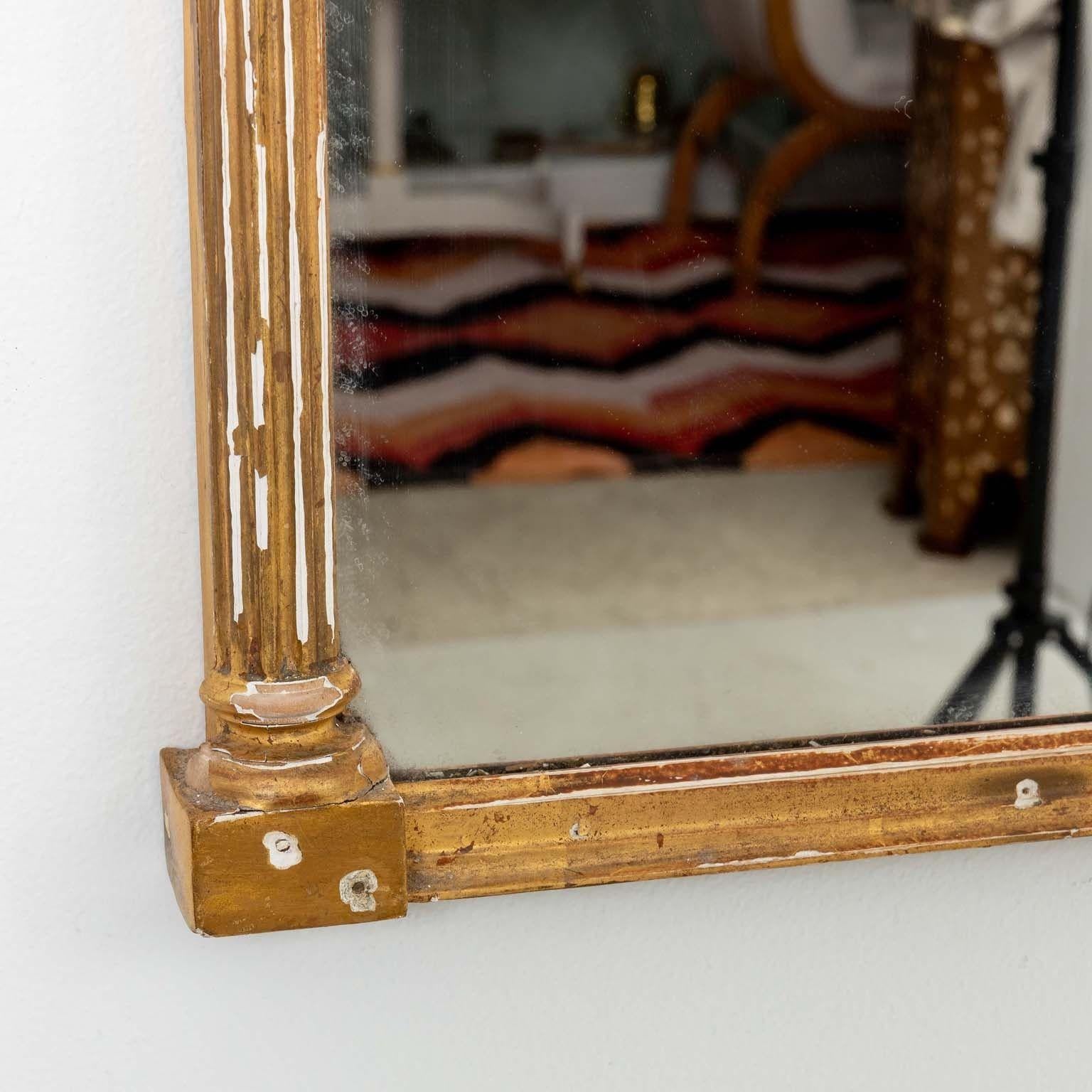 An early 20th Century Federal style mirror, a regal testament to timeless design, adorned with pineapple finals—a symbol of hospitality and warmth. Its pediment boasts a captivating eglomise panel, gracefully shaped to echo the frame. Delicate