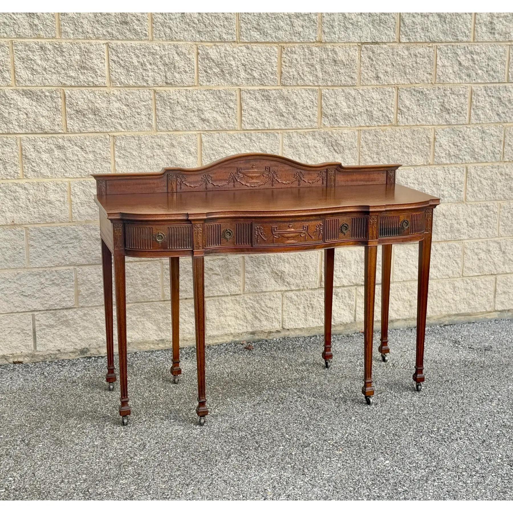 The sideboard features detailed carvings on the back panel and three drawers with original brass hardware. It stands on fluted legs with spade feet and includes a curved backsplash that adds height and character.