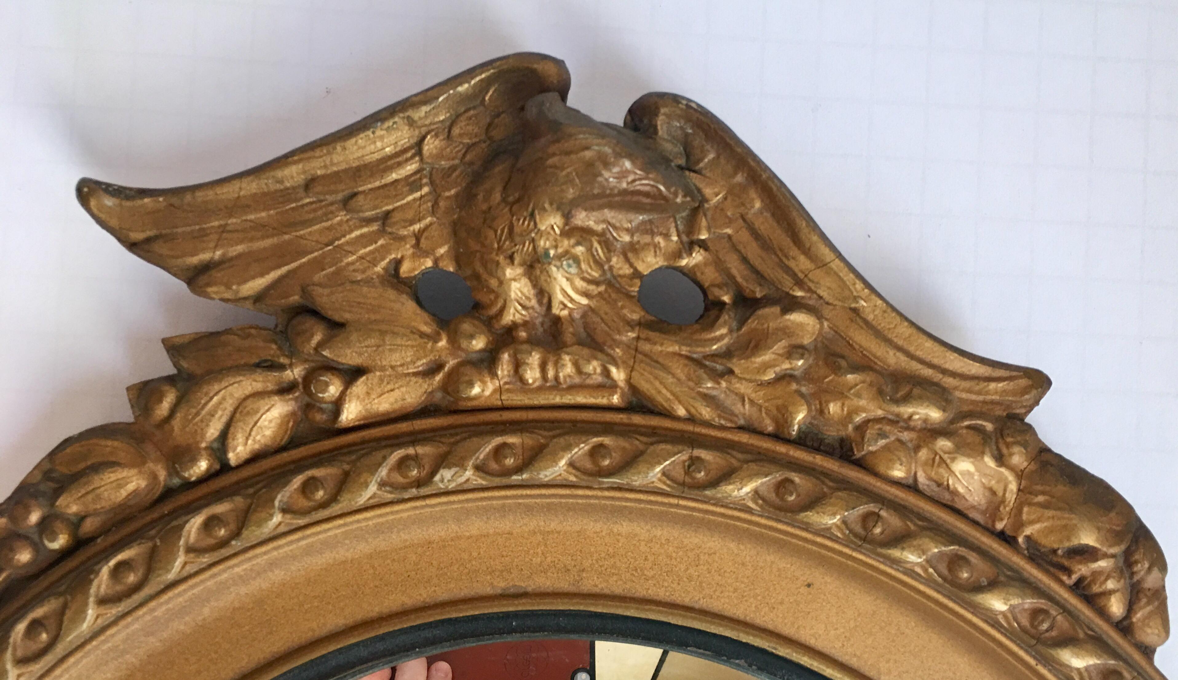 Midcentury round convex giltwood wall mirror featuring a carved eagle with acanthus foliate decoration. This sculptural Regency style convex fish eye eagle mirror is a nice size to incorporate into an art grouping.