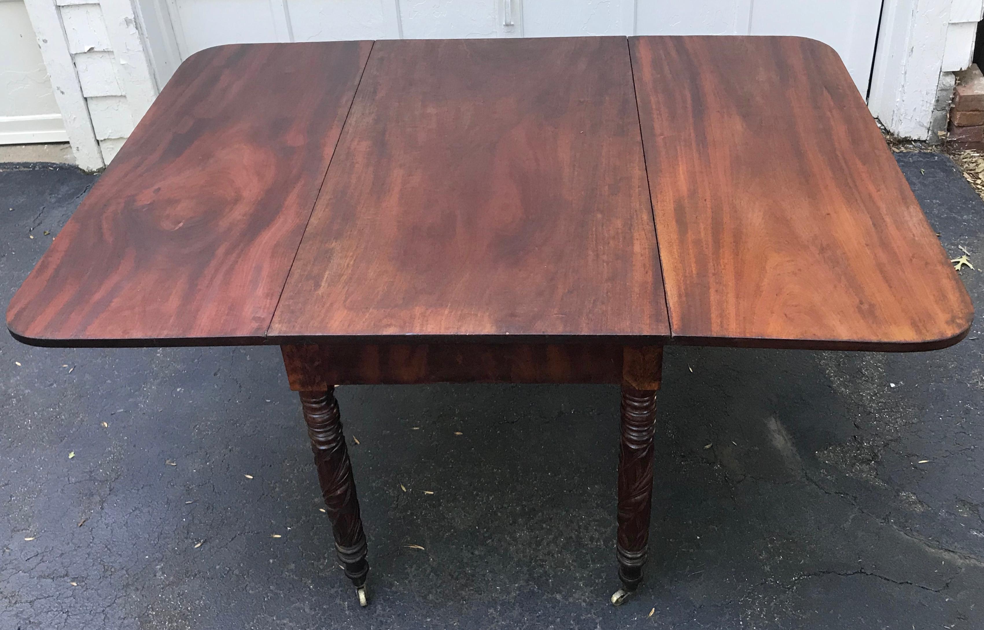Federal Tobacco leaf carved leg table. Late Federal / American Empire mahogany drop-leaf table with hand carved tobacco leaf legs on original brass casters supporting a commodious central board with drop leaves. Dining table is 42