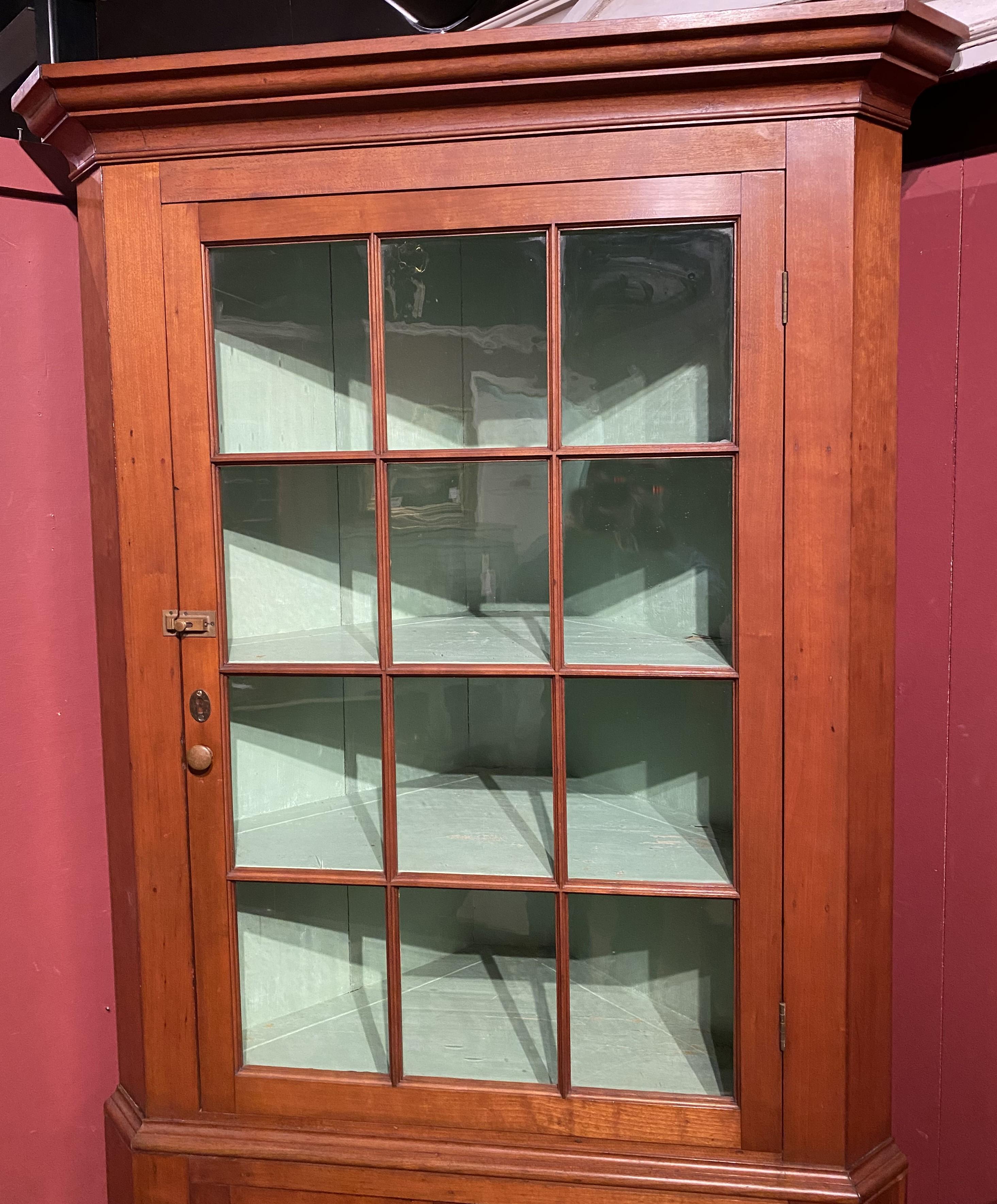 A fine example of a Federal two part corner cupboard, its upper case with a single glass door, opening to a light green painted interior with two shelves, over a lower case with two blind paneled doors, opening to a single shelf storage compartment,