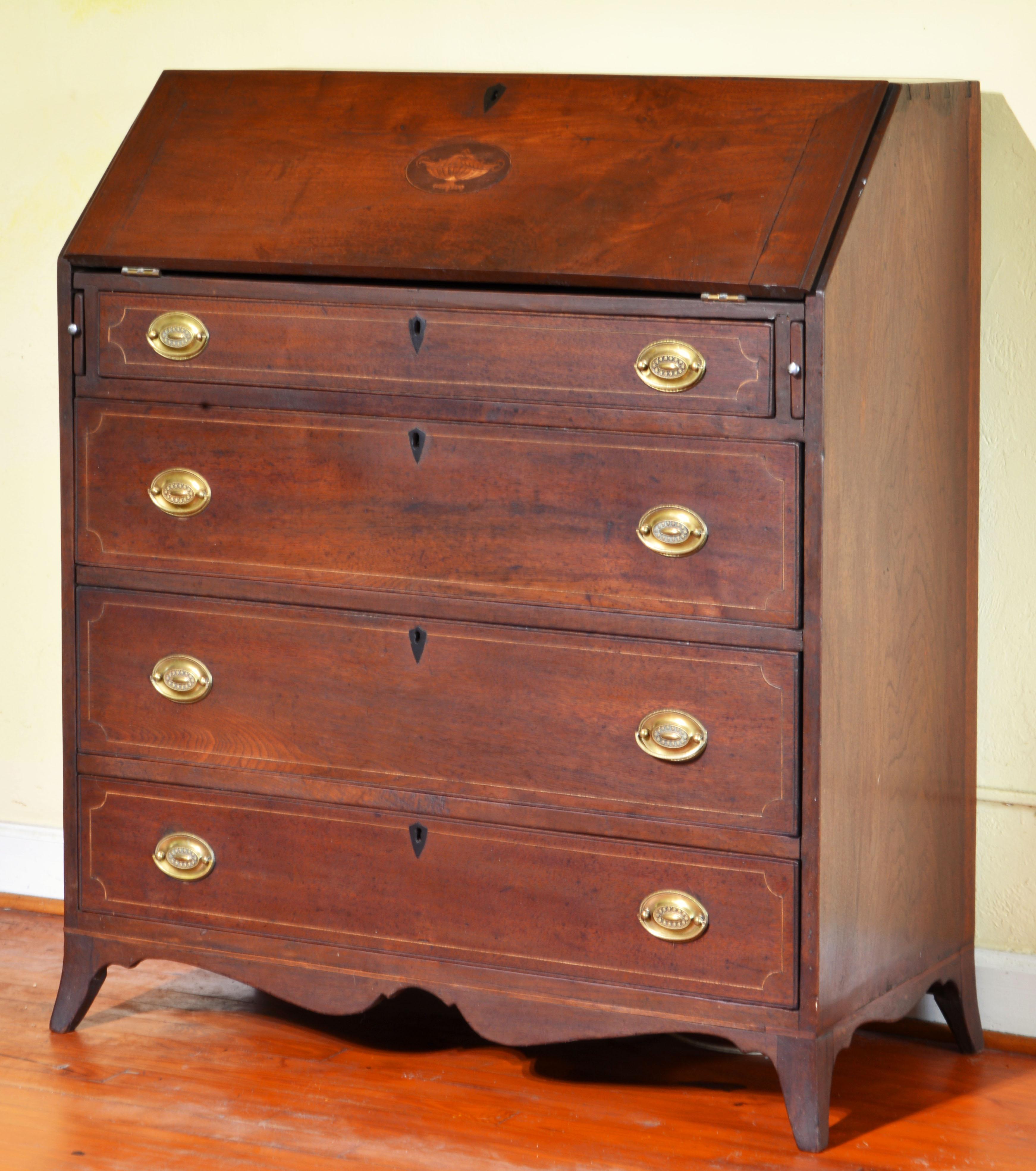 This Southern Federal solid walnut desk, dating to circa 1800-1820 and made in the Piedmont Region of Virginia, features a stringed slant front centering an inlaid classical style motif that opens up to an interior fitted with pigeon holes and four