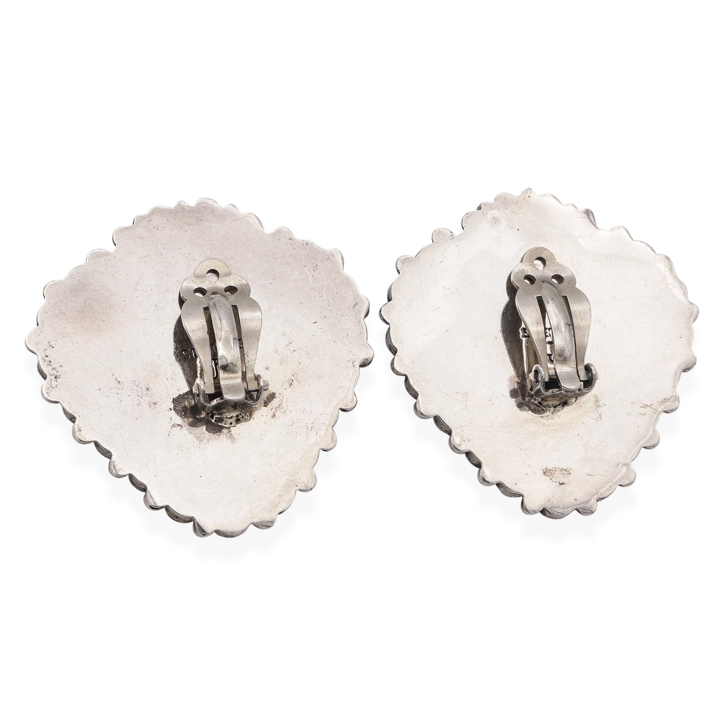 These striking vintage Southwestern clip-on earrings are a bold celebration of artisan craftsmanship and regional heritage. Signed “JF,” each earring showcases a heart-shaped mosaic of vibrant turquoise inlays, meticulously set in sterling silver.