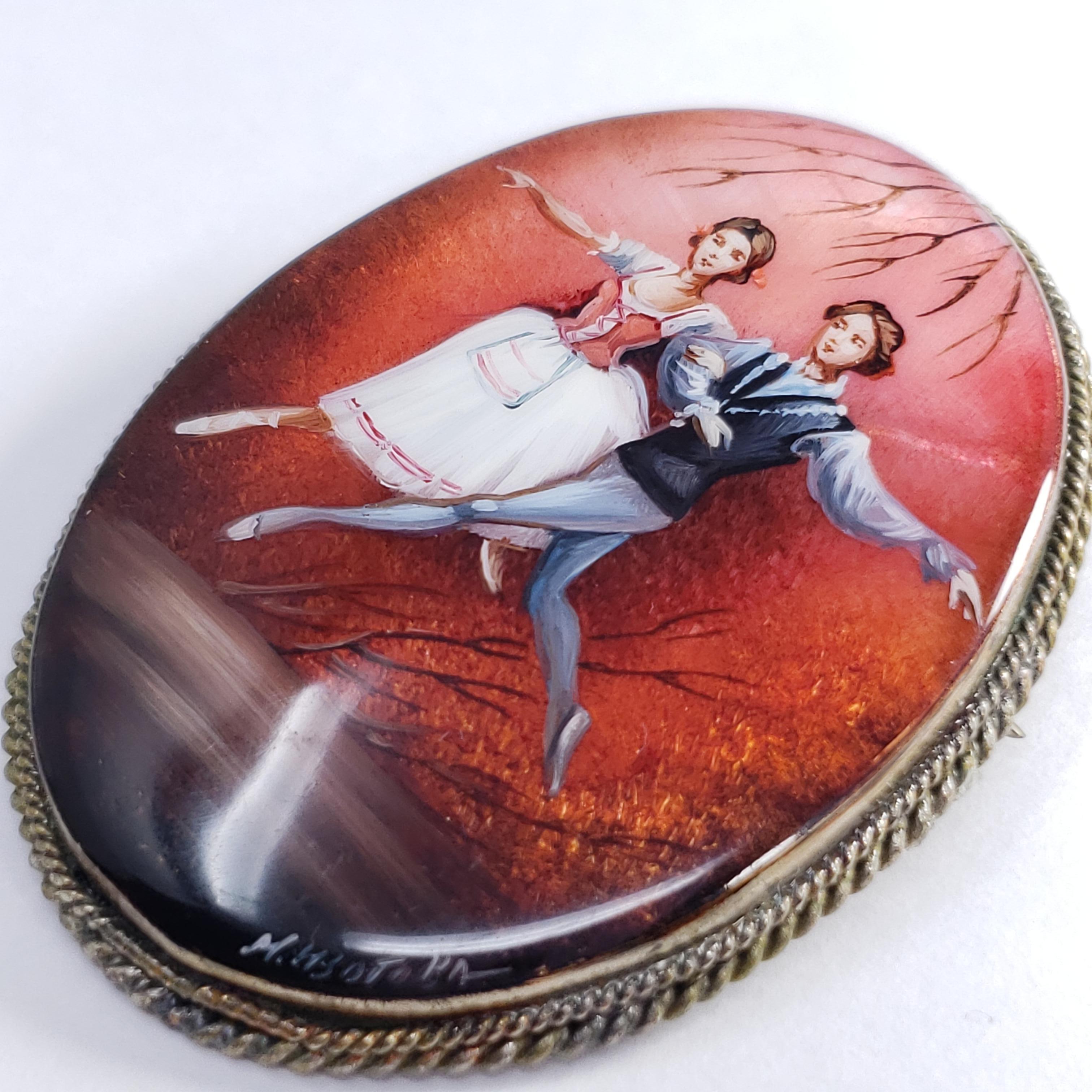 Une exquise broche russe Fedoskino sertie dans une belle lunette en argent allemand. Présente un couple de danseurs sur un fond rouge, peint à la main sur une pierre de nacre avec une couche de laque.

Signé par l'artiste - M Izotova (М
