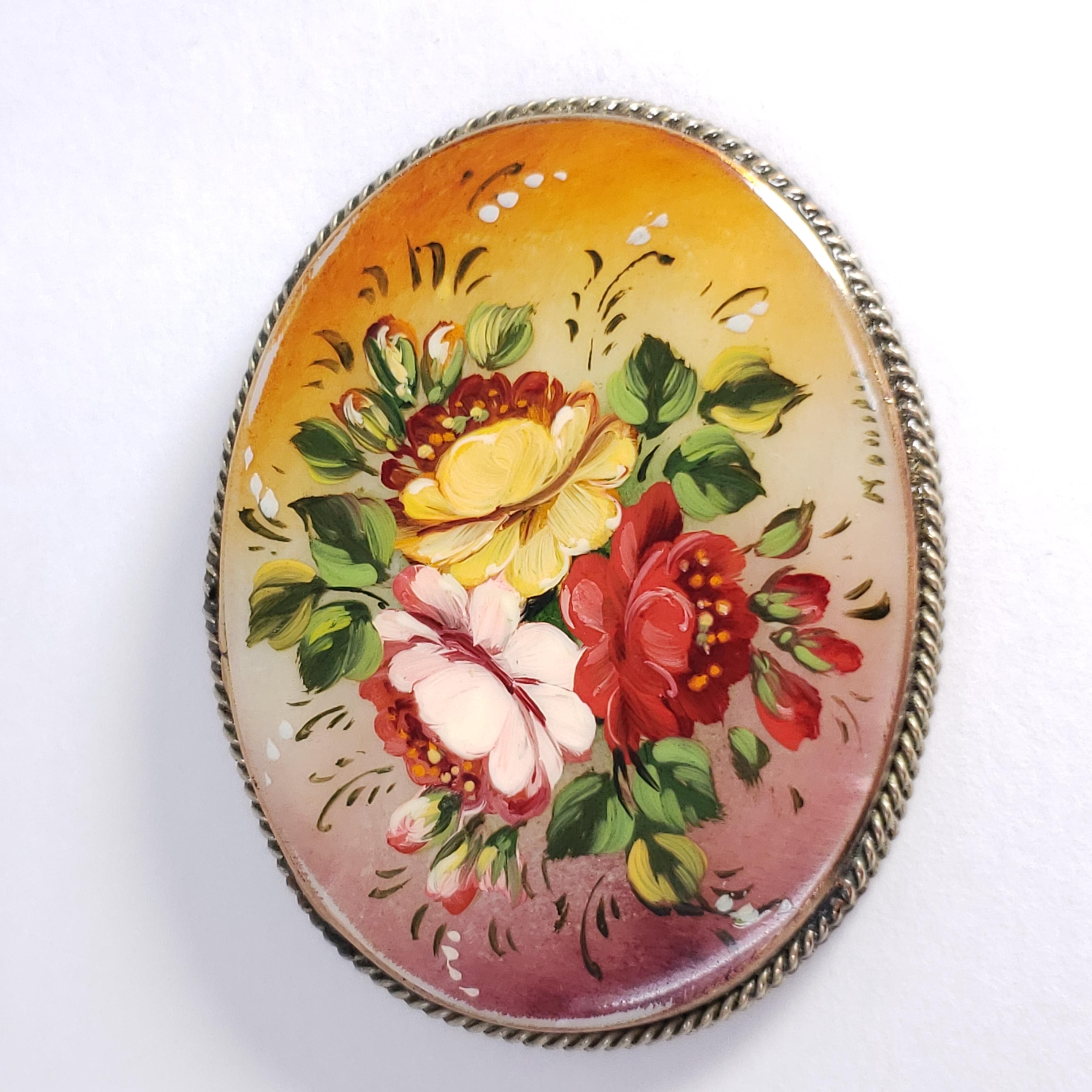 An exquisite Russian Fedoskino brooch set in a beautiful German silver bezel. Features a hand painted bouquet of bright, vibrant flowers on a mother-of-pearl stone covered with a layer of lacquer.

Signed by artist.

Circa early 1900s