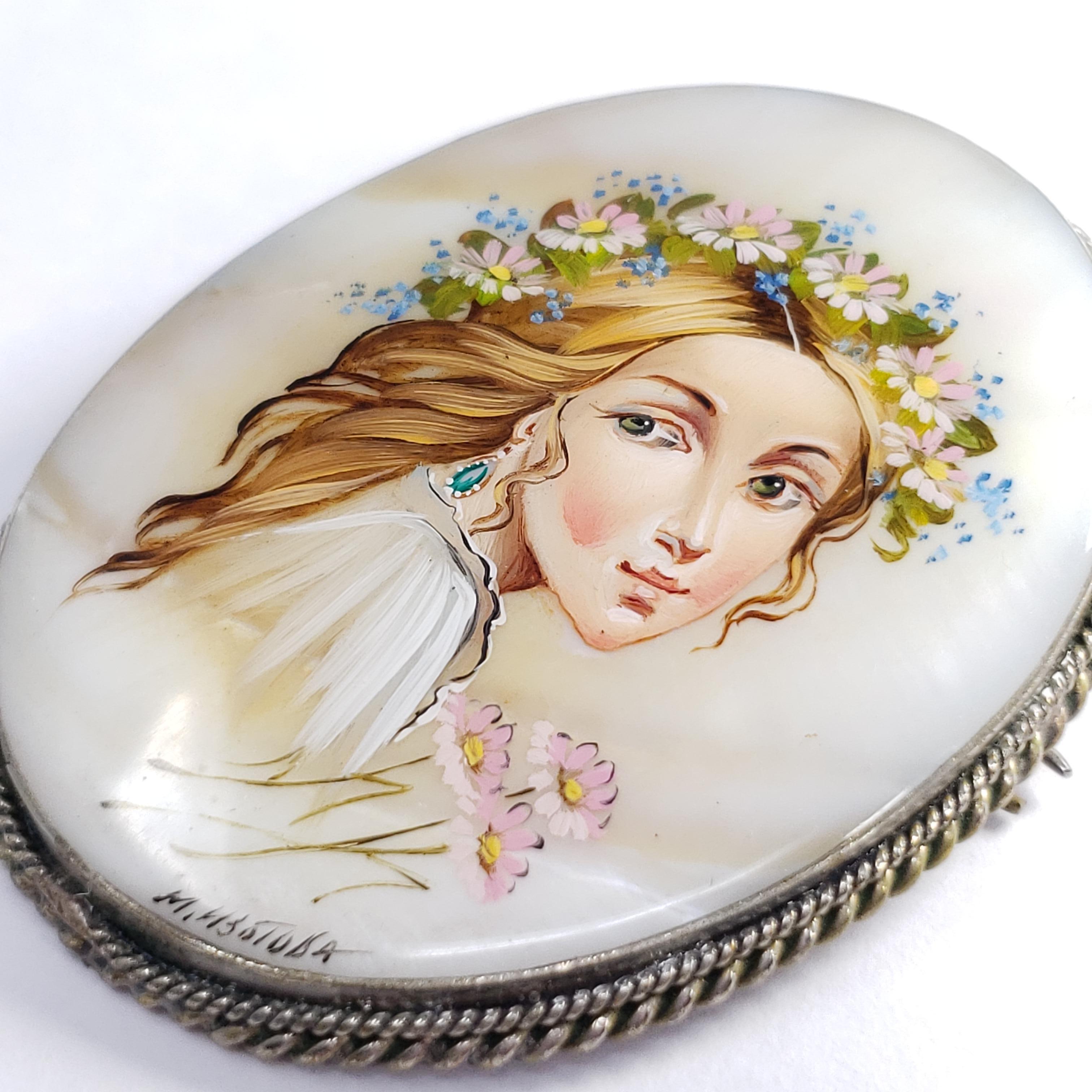 An exquisite Russian Fedoskino brooch set in a beautiful German silver bezel. Features a likeness of a beautiful woman in a floral head wreath, hand-painted on a mother-of-pearl stone with a layer of lacquer.

Signed by artist - M Izotova (М