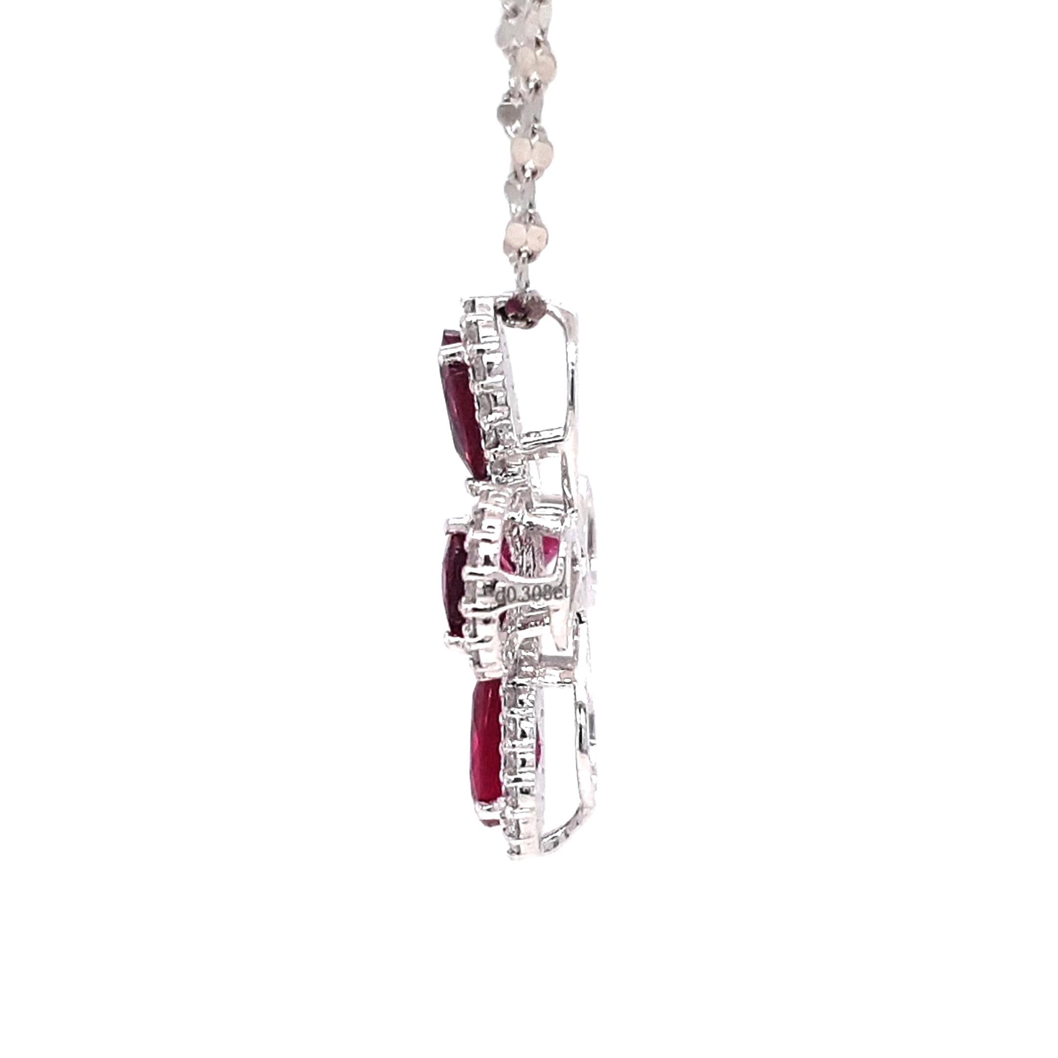 Ce collier pendentif exquis présente un motif de croix harmonieux, où cinq rubis vifs - quatre en forme de poire et un rond - rayonnent à partir d'un axe central, chacun entouré d'un halo de diamants taillés en brillant. Serti dans un platine