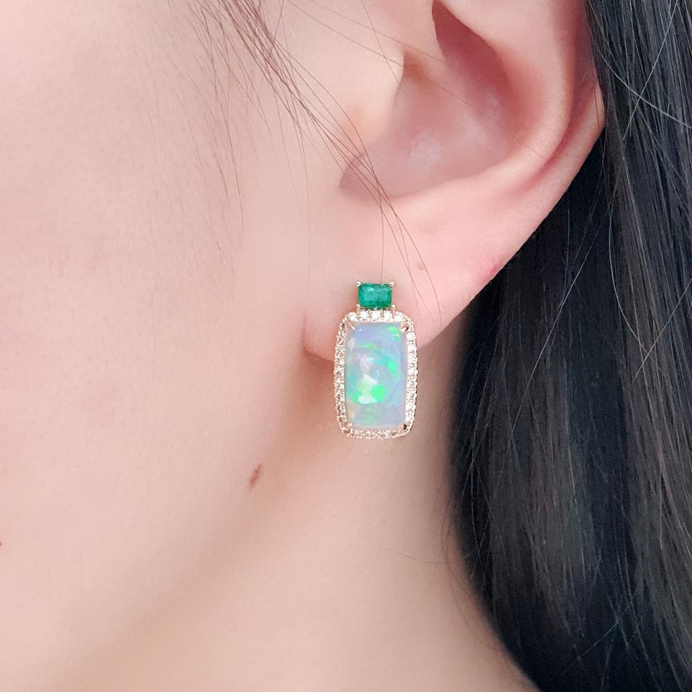 Crafted in 14ct yellow gold, these elegant drop earrings pair luminous rectangular opals — alive with flashes of green, blue, red, and yellow — with vivid emeralds and a halo of pavé-set diamonds, creating a captivating interplay of colour and light