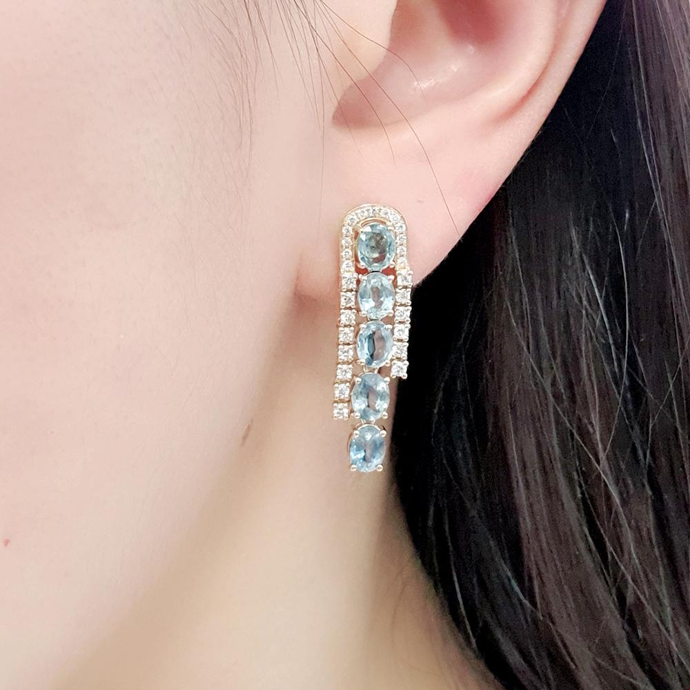 Crafted in rich yellow gold, these striking earrings showcase six vari-hue oval-cut blue sapphires in a graceful vertical setting, each encircled by a glittering border of pavé-set diamonds — a timeless cascade of elegance and brilliance that brings