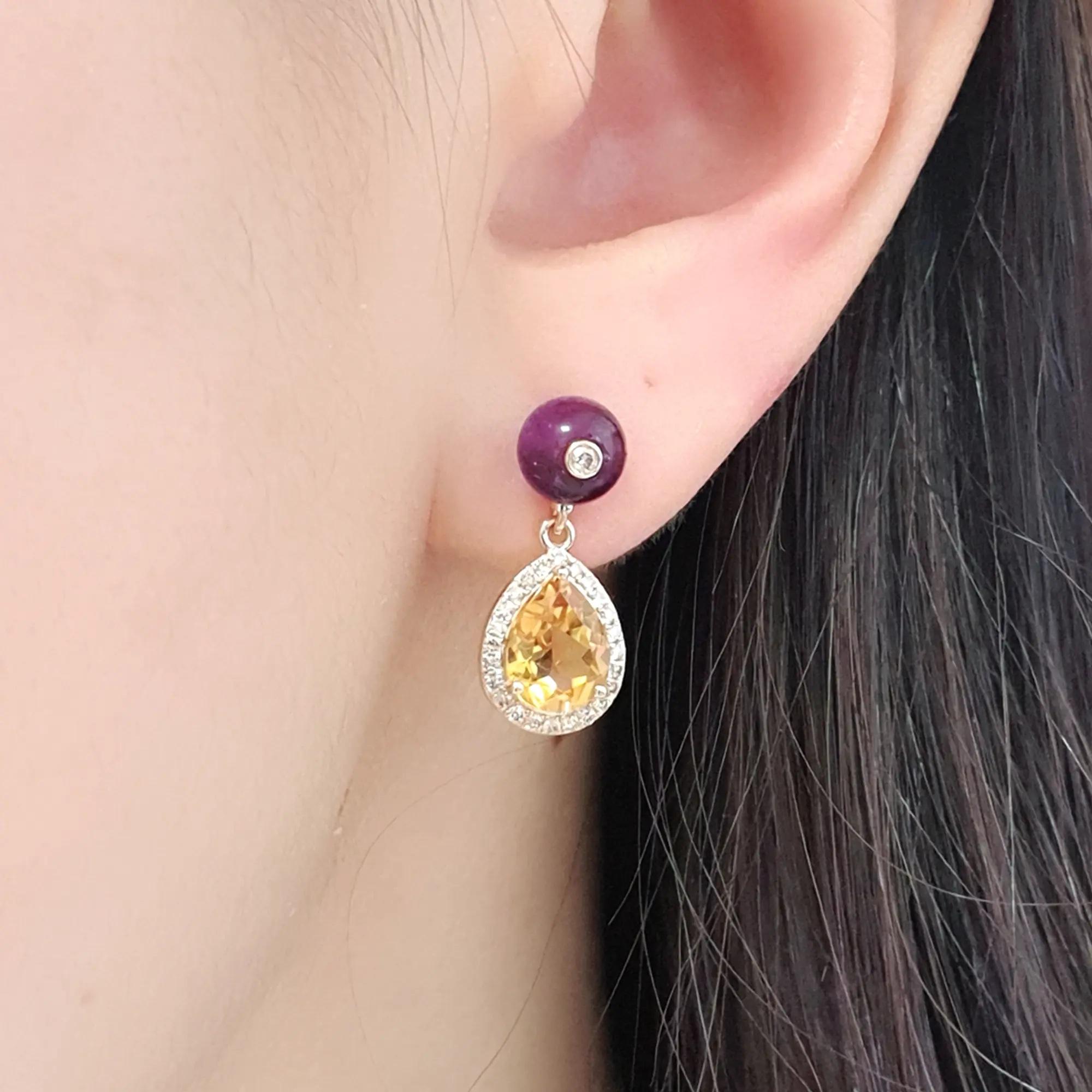 Eleva la tua collezione di gioielli con questi squisiti orecchini a goccia in oro giallo 14ct, progettati per affascinare con il loro fascino aggraziato e le loro gemme vibranti. Ogni orecchino presenta una perla di ametista lucida, coronata da un
