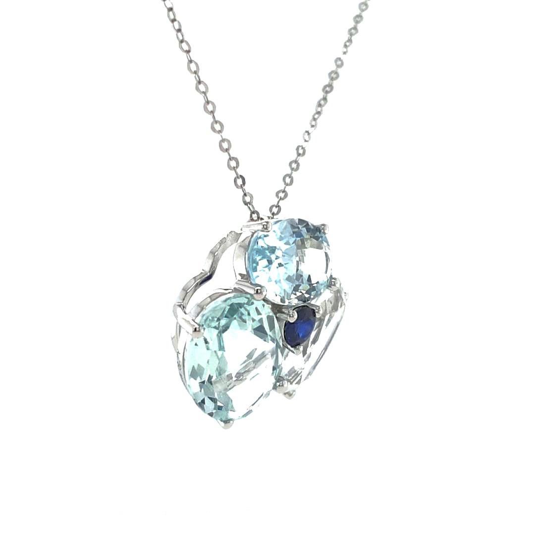 Crafted in luxurious 18ct white gold, this enchanting pendant features a deep blue sapphire at its core, weighing 0.28ct. Surrounding it are three oval-cut aquamarines delicately set at an angle to enhance their brilliance. Suspended gracefully from
