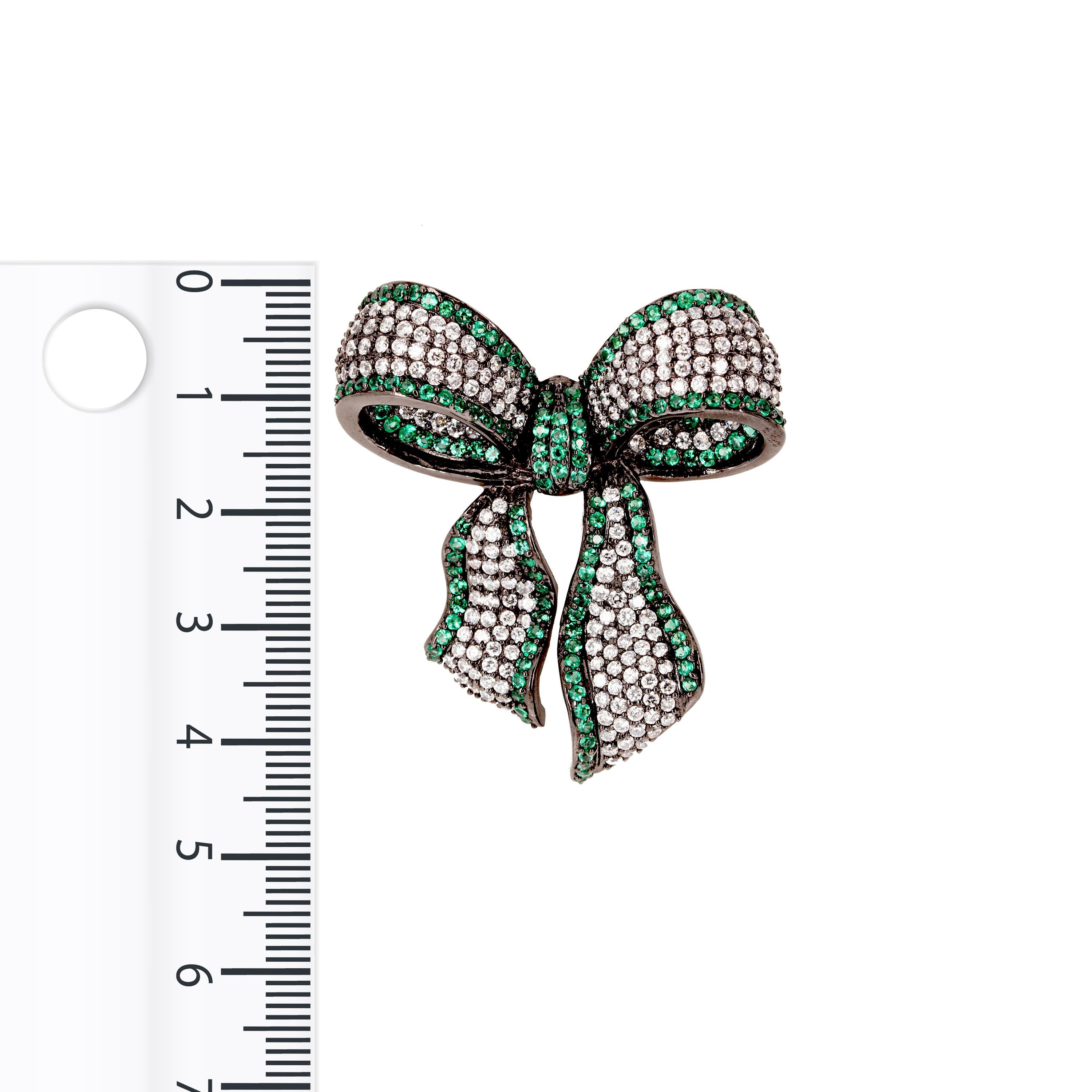 Tie up your outfit with a bedazzled ribbon bow. The classic bow motif is conveyed through a feminine sculptural silhouette and vibrant coloured gemstones, featuring white cubic zirconia hemmed with emerald green cubic zirconia, set in black