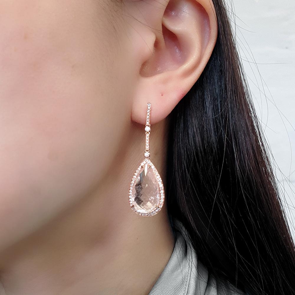 A unique pair of earrings adorned with nature's exquisite gemstones: morganite and diamonds. Crafted in the warm hues of 18ct rose gold, each earring showcases an 11.90ct briolette-cut pear-shaped morganite, encircled by a halo of glistening