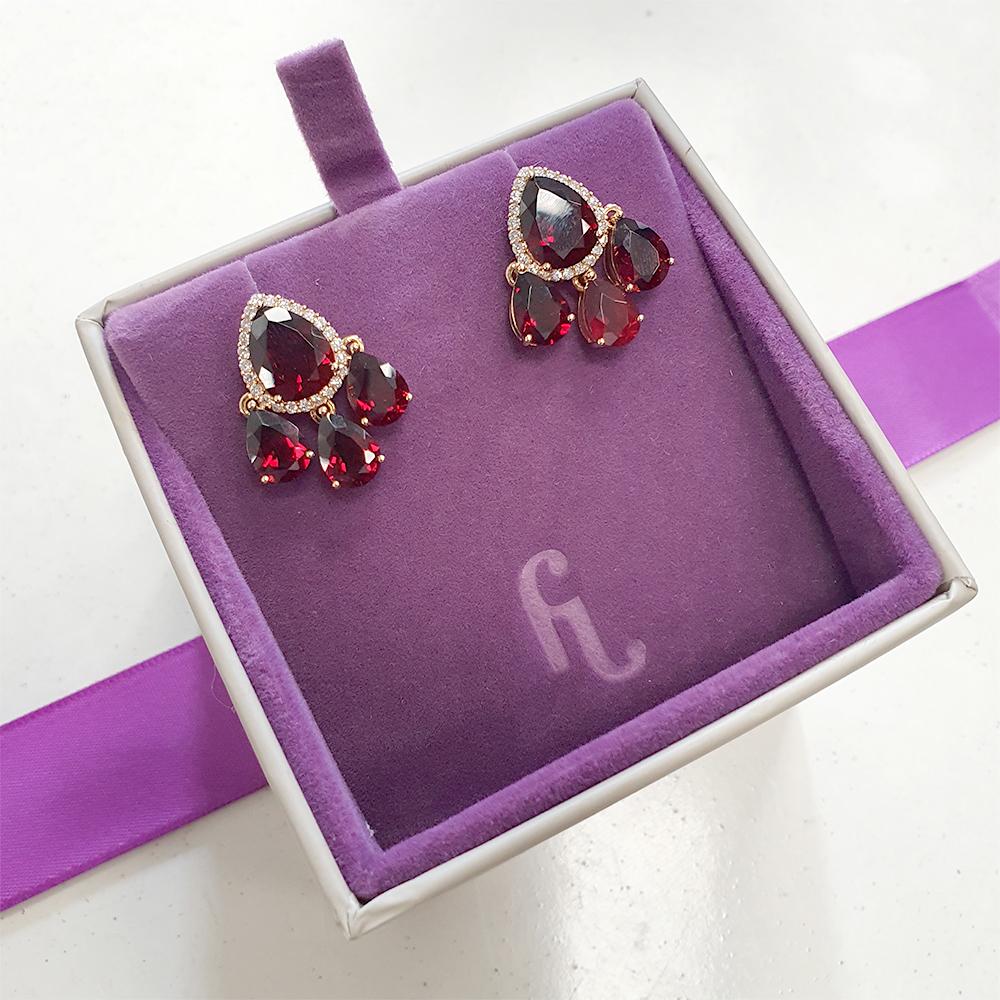 Diese exquisiten Tropfenohrringe sind der Inbegriff von Eleganz und Raffinesse. Jeder Ohrring besteht aus einem atemberaubenden Granat im Birnenschliff, der von einem Halo aus Diamanten im Brillantschliff umrahmt wird. Die Ohrringe sind mit drei