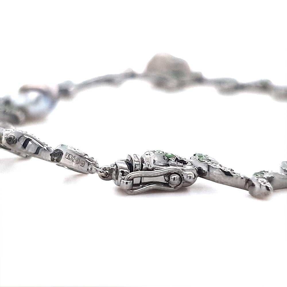 This exquisite bracelet from the Whispering Collection is crafted in 18ct white gold with black rhodium plating, featuring crescent motifs adorned with vibrant tsavorites and brilliant diamonds. Lustrous baroque freshwater pearls in deep iridescent