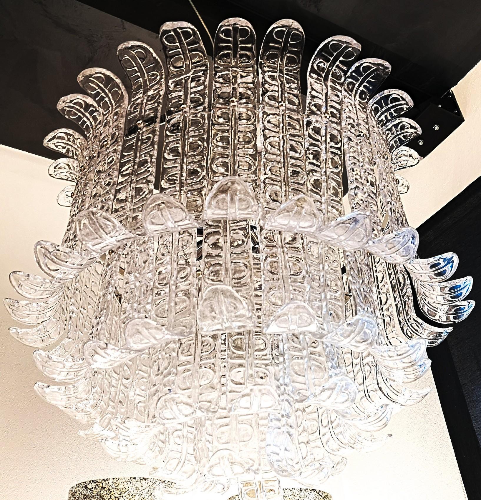 Great midcentury chandelier. Four tiers of Felci elements to tightly fence the bulb and the hardware.
Clear glass for a greater light output, the design on the leaves amplifies the reflection.

Piastra technique. Murano clear glass is poured over