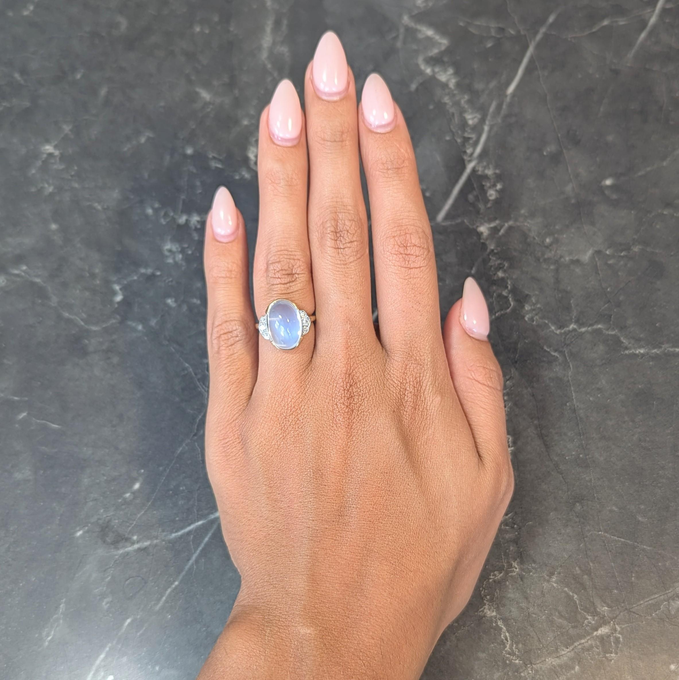 Centering an oval-shaped domed moonstone cabochon measuring 10.0 x 15.0 mm 
Translucent colorless body with vivid blue adularescence - set in semi bezel
Flanked by fanning white gold cathedral shoulders bead set with diamonds
Old European cut and