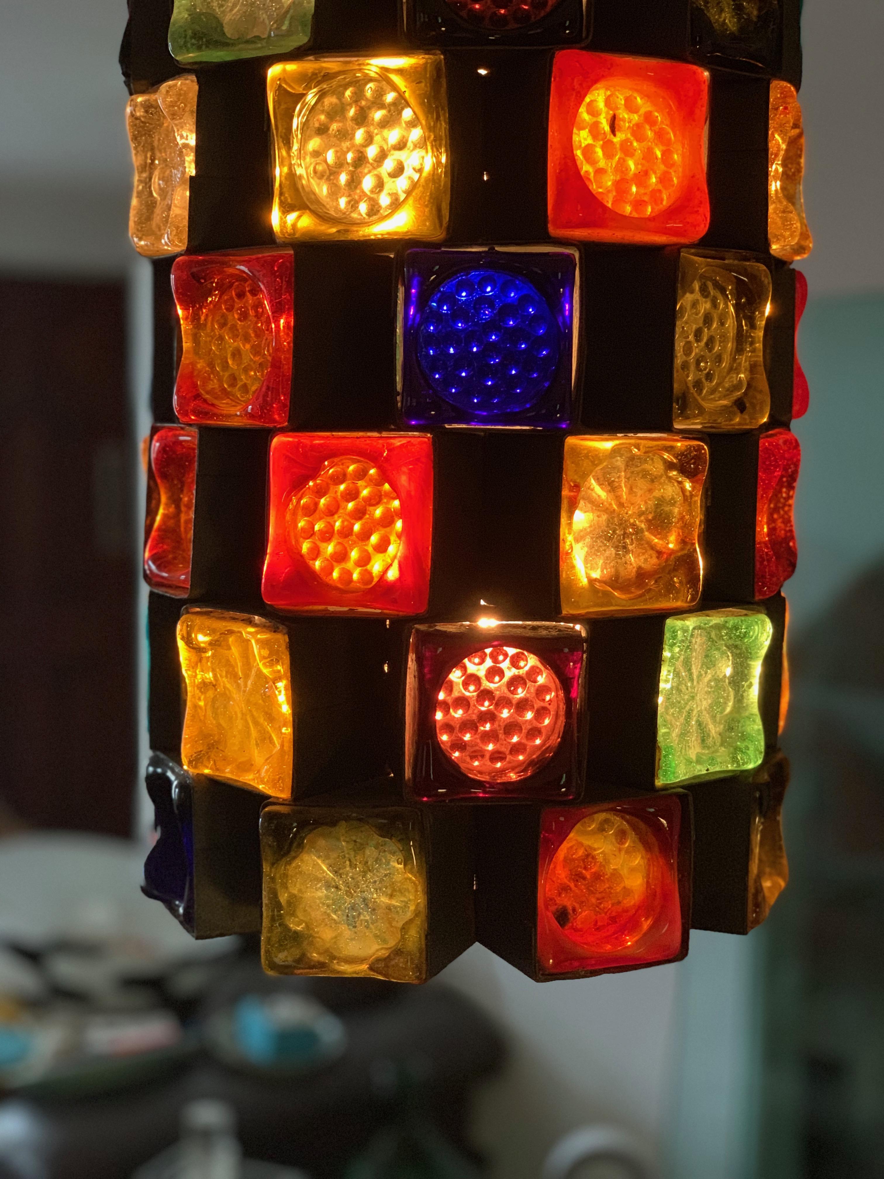 Midcentury Brutalist or forged metal and stained glass pendant light fixture by Felipe Delfinger for Feders, 1970s Latin American Modern.

Stained glass cubes with uniquely patterned surfaces, each in its own forged metal pod, set together as a