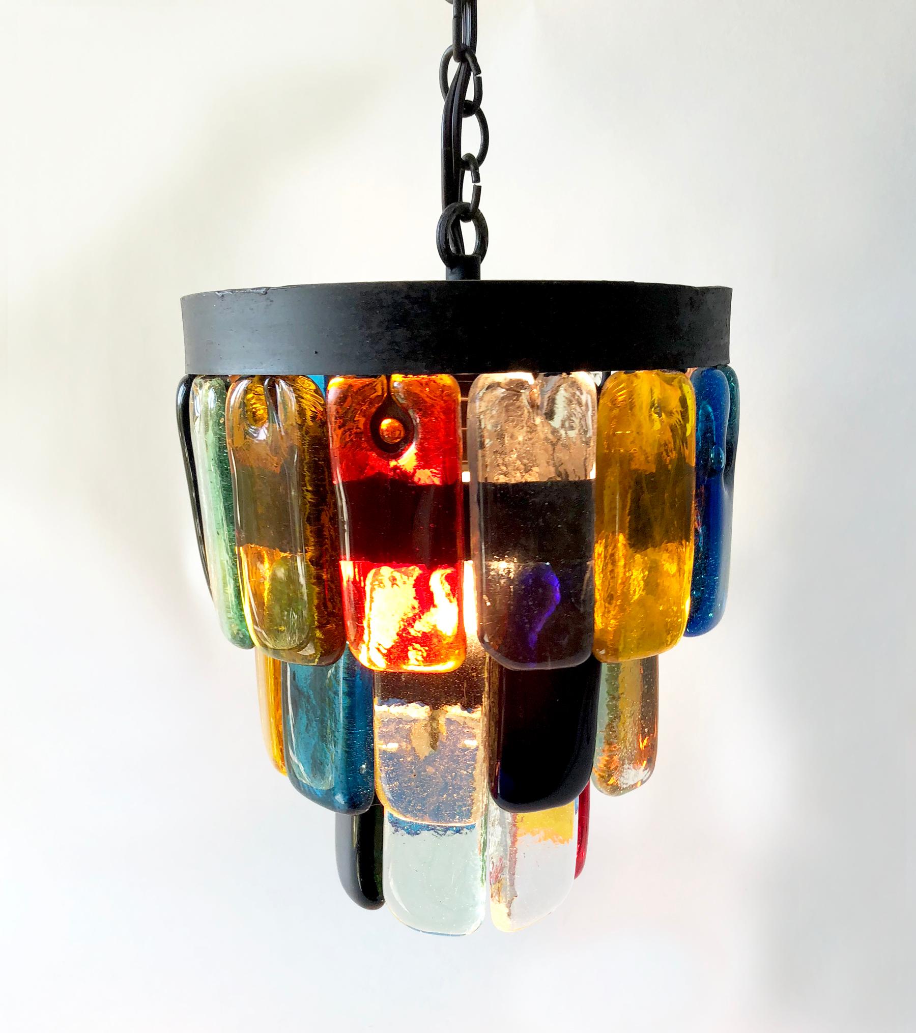 Mexican modern glass and iron hanging pendant lamp designed by Felipe Delfinger for Feders. Lamp is comprised of three tiers of multicolored glass panels attached to iron rings suspended with inner chains. Measuring 10