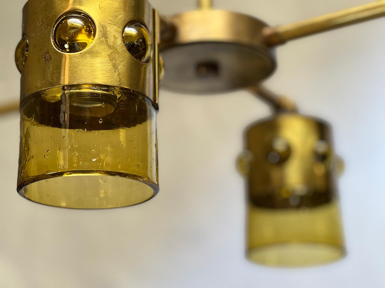 Four Brutalist glass shades are original Felipe Derflinger blown caged glass drinking glasses. They have been drilled and converted to become light shades on this four light brass chandelier.
Chandelier and wiring are brand new, aged to Brutalist