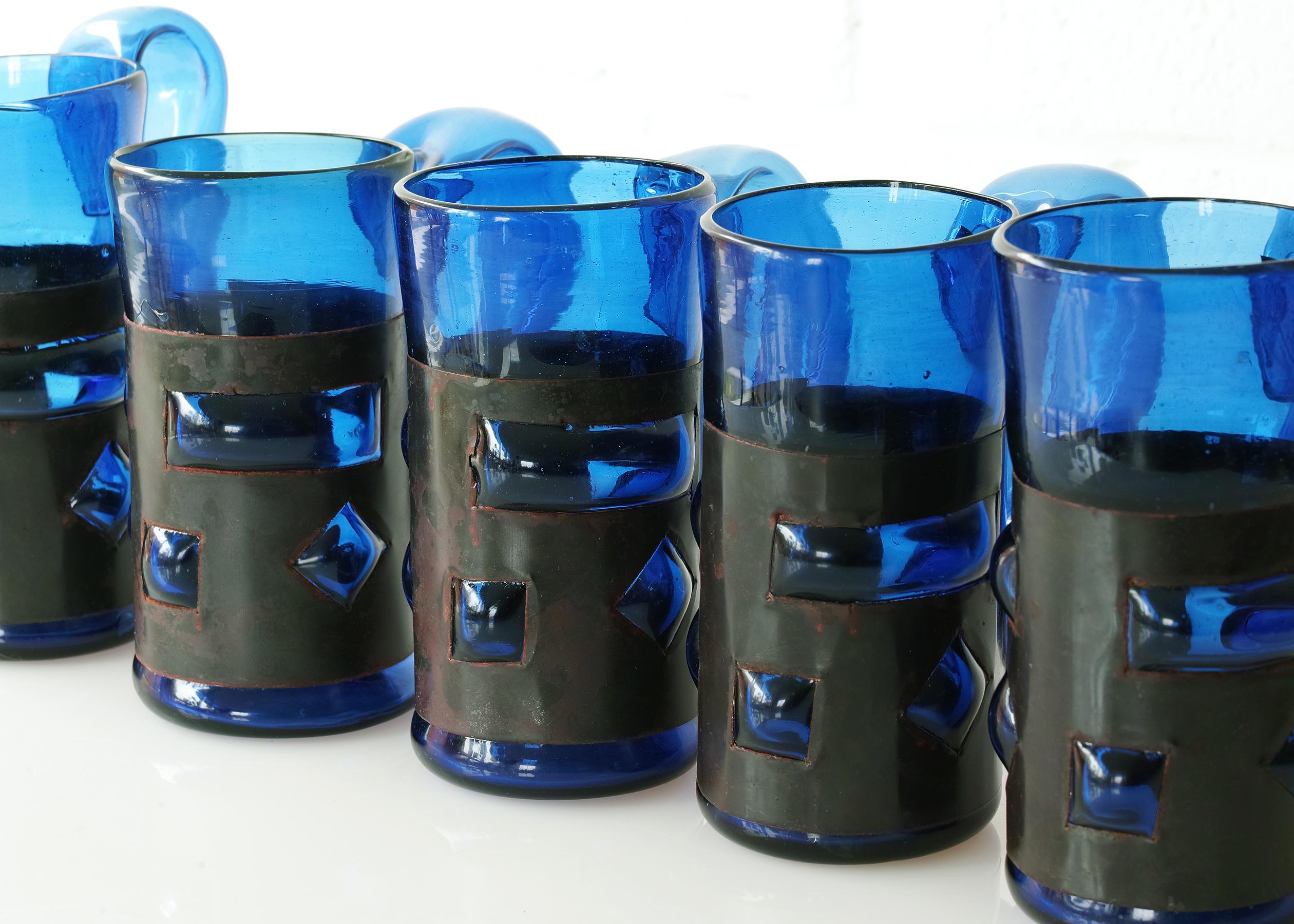 For your consideration is this fine set of imprisoned glass tankards by Felipe Derflingher for Feders, Mexico. The glass is mouth blown from recycled blue glass into sheet metal cages with cutouts through which the glass bulges. Each tankard is