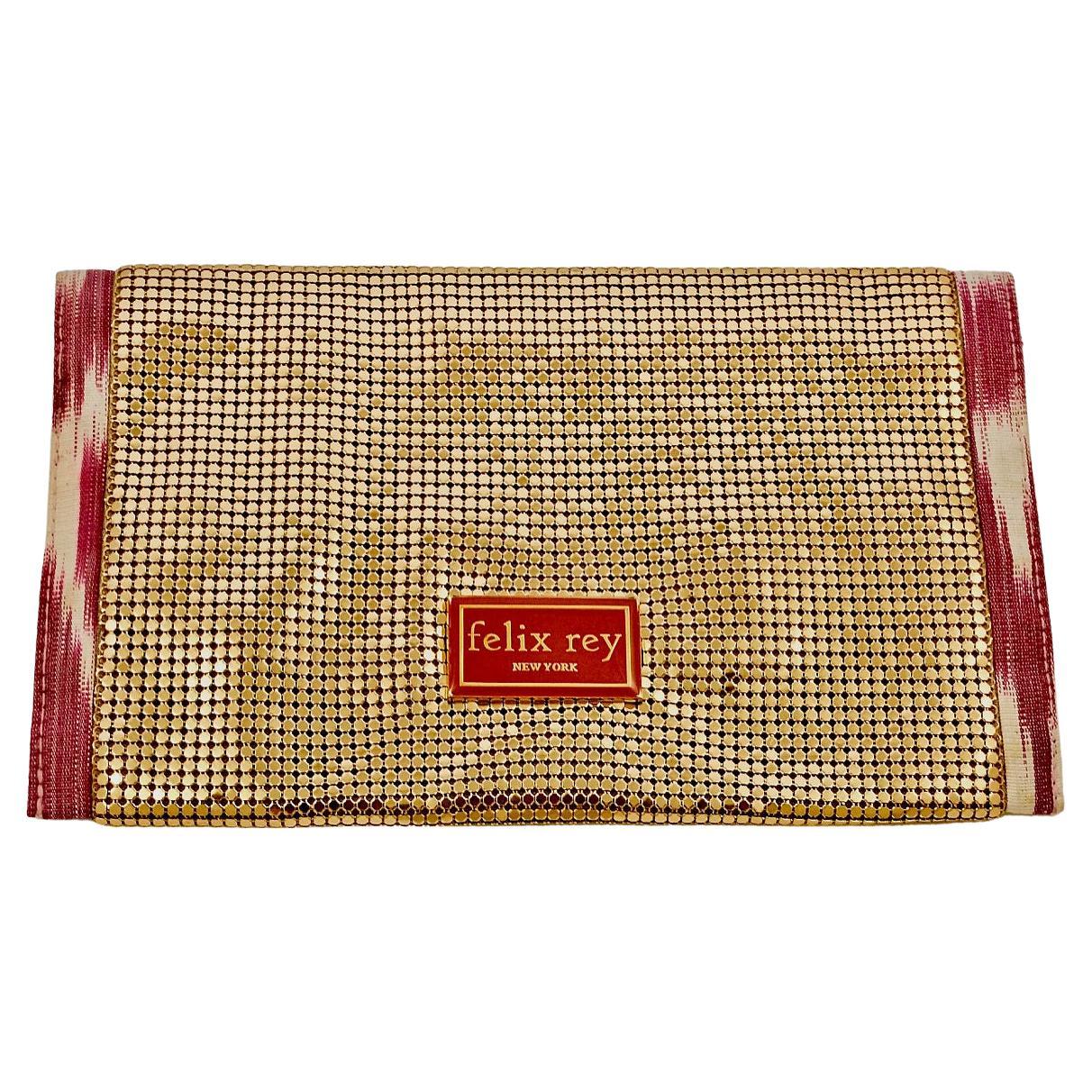 Magnifique pochette Felix Rey New York en maille dorée avec bordure en tissu ikat rose et blanc, et double fermeture magnétique. Mesure la largeur 22.8 cm / 8.9 inches et la hauteur 14 cm / 5.5 inches. A l'intérieur, il y a une jolie doublure en