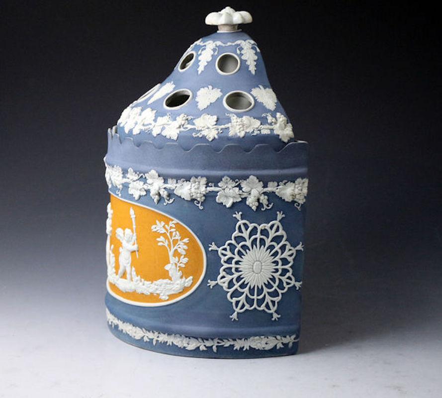 Dated: 1810 Burslem Staffordshire England

A Jasperware felsparic bodied bough pot of superior quality with an elaborate dome cover with a flower finial. The decoration of the center panel shows two winged cherubs at play modeled on a dark orange