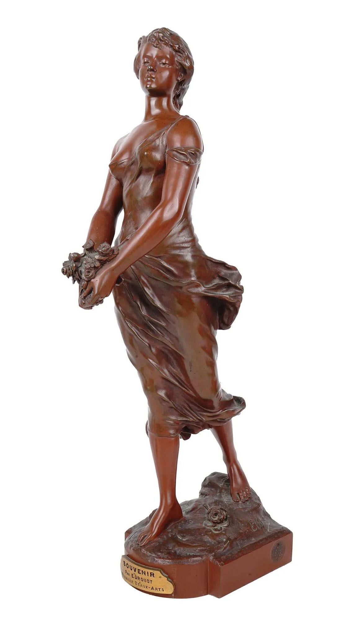 Our patinated bronze figurine of a lovely female holding a bouquet of flowers after Edouard Drouot (1859 - 1945) is entitled Souvenir. Base carries a plaque that carries the title and artist's name and Medaille de Beaux-Arts, no doubt a reference to