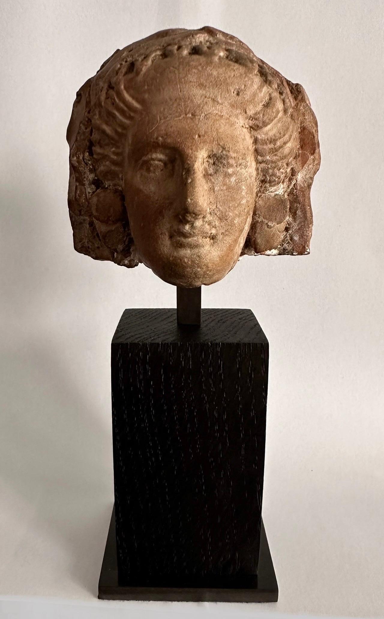Female statuette head, terracotta.
Magna Graecia, 4th century before Christ.

It is topped with a wide headband around with strands and wrapped.
Circular earrings.
Wood and bronze base.
Thermoluminescence test.

Head height: 6,8 cm.
Overall: 16,6 cm.