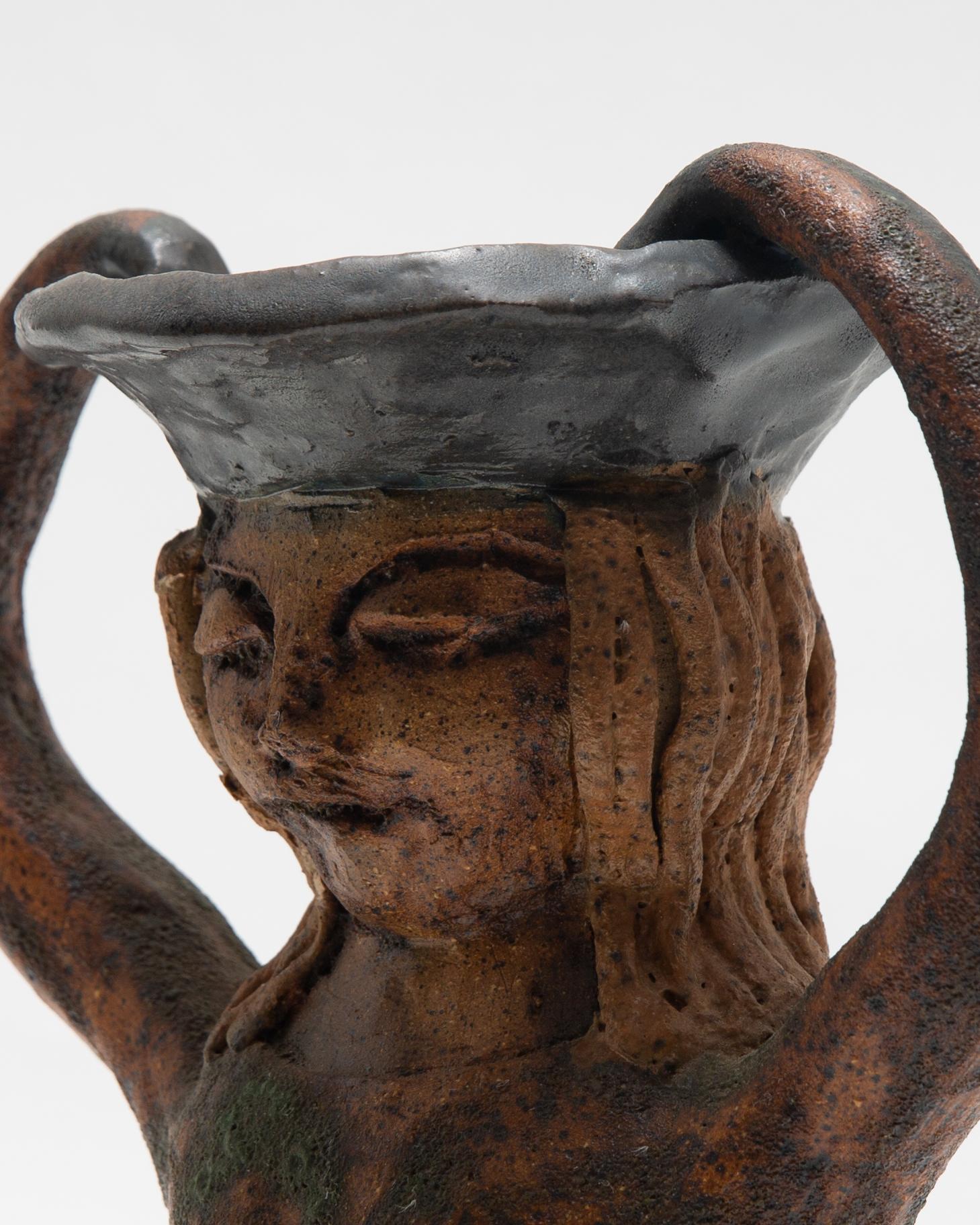 Precioso jarrón de cerámica hecho a mano de una mujer tranquila que sostiene lo que parece ser su sombrero. La profundidad del jarrón es toda la longitud del torso de la mujer. El esmalte es extremadamente singular: el torso parece tener altibajos
