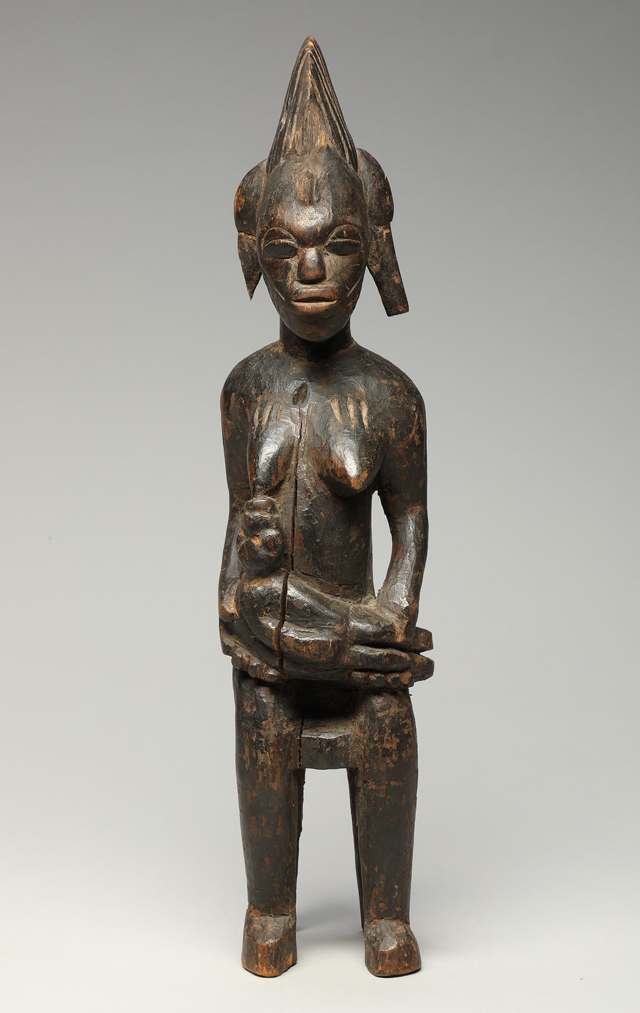 Figure féminine de maternité en bois sculpté de Senufo, assise sur un tabouret, avec un bébé sur les genoux qui se lève pour le nourrir.  Représente la mère qui nourrit la communauté.
La figure mesure 17 pouces de haut.


