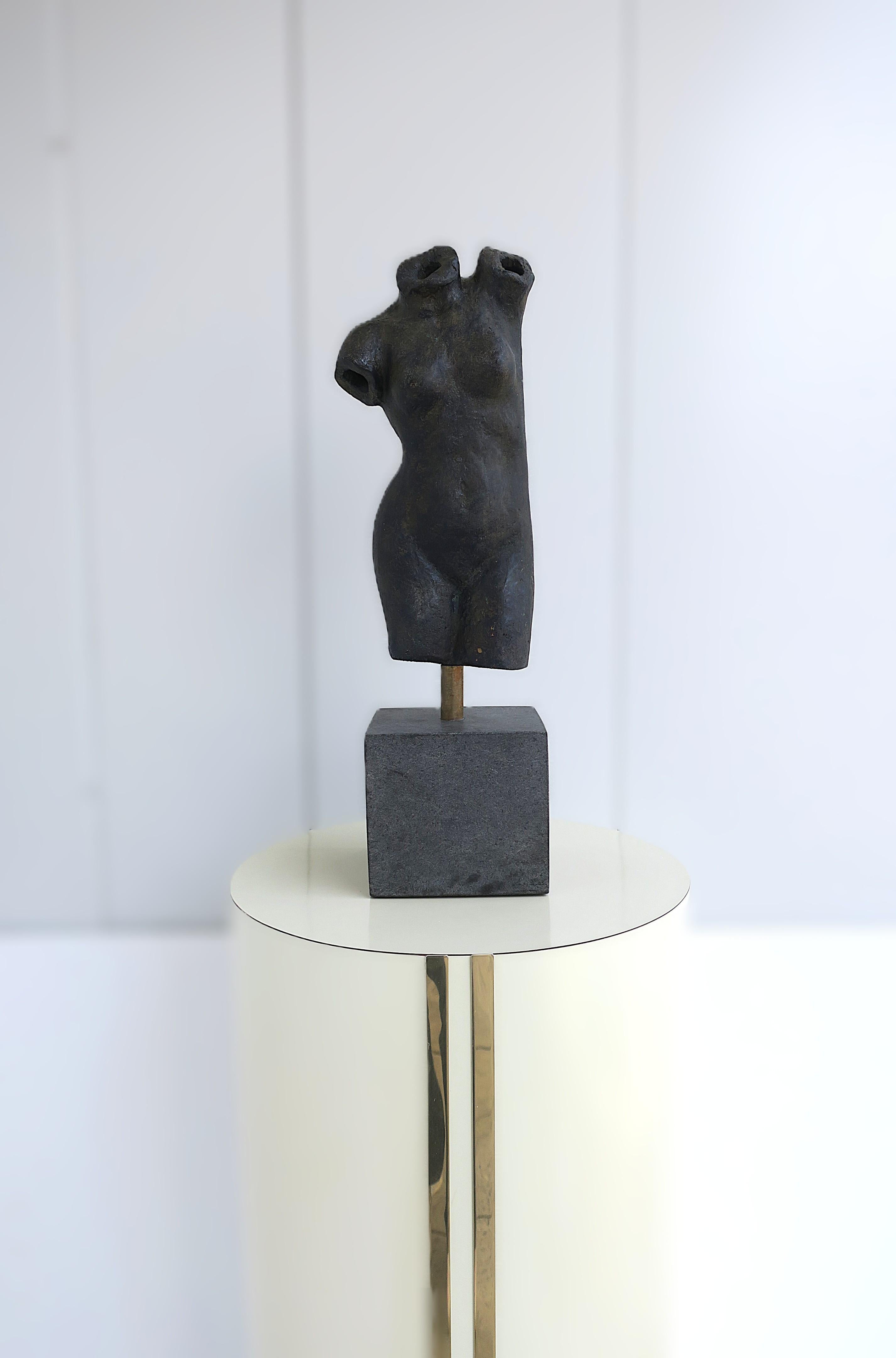 A substantial female torso sculpture from designer Kelly Wearstler. This female nude torso sculpture is metal in a dark charcoal gunmetal hue with traces of a light gold blended accent, supported (attached) by a brass rod and stone base. Brass