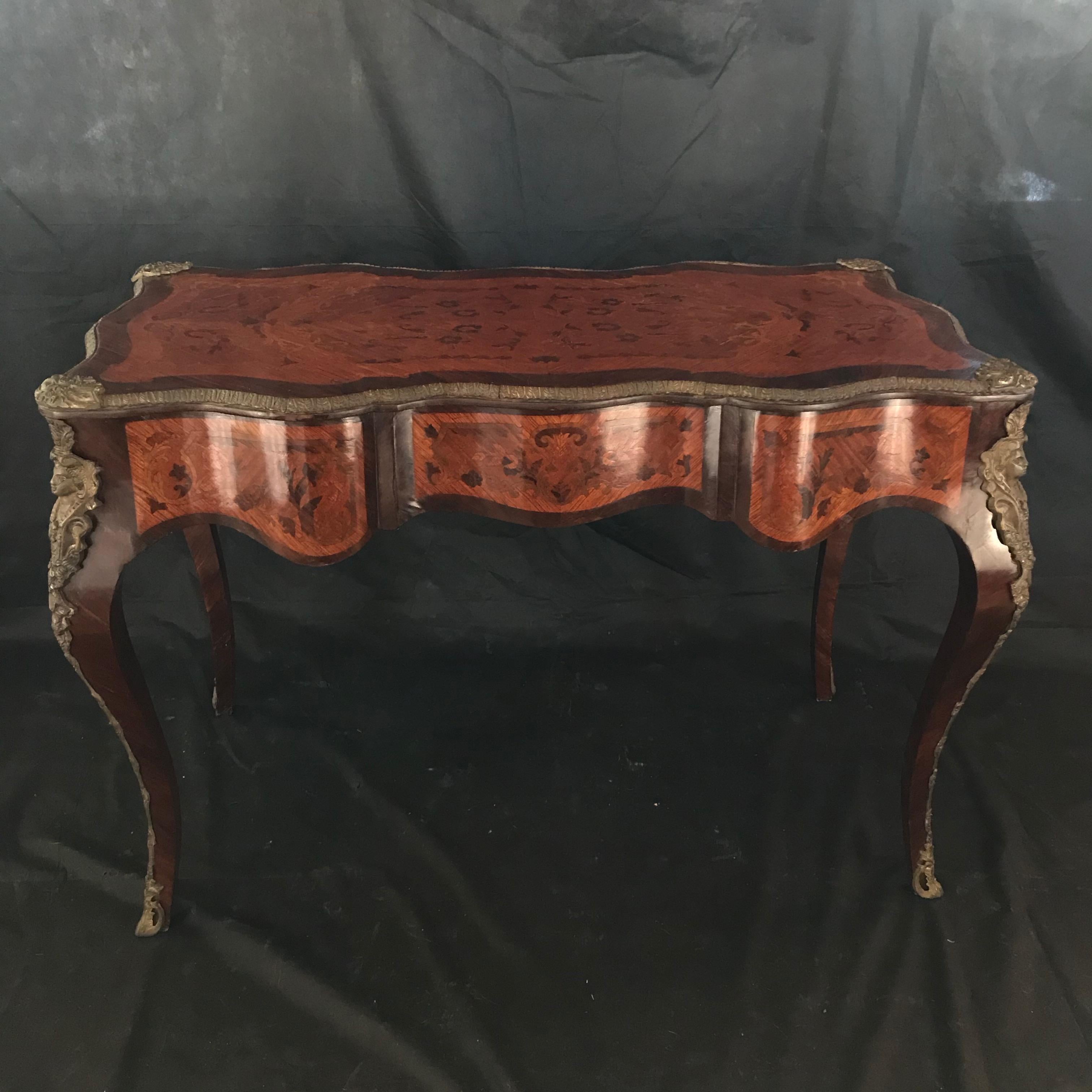 French Louis XV style mahogany and fruitwood marquetry desk for an aristrocratic lady having heavy solid bronze figural corners that lead to curved legs with bronze framing and bronze sabots. There are three drawers on the front supporting a