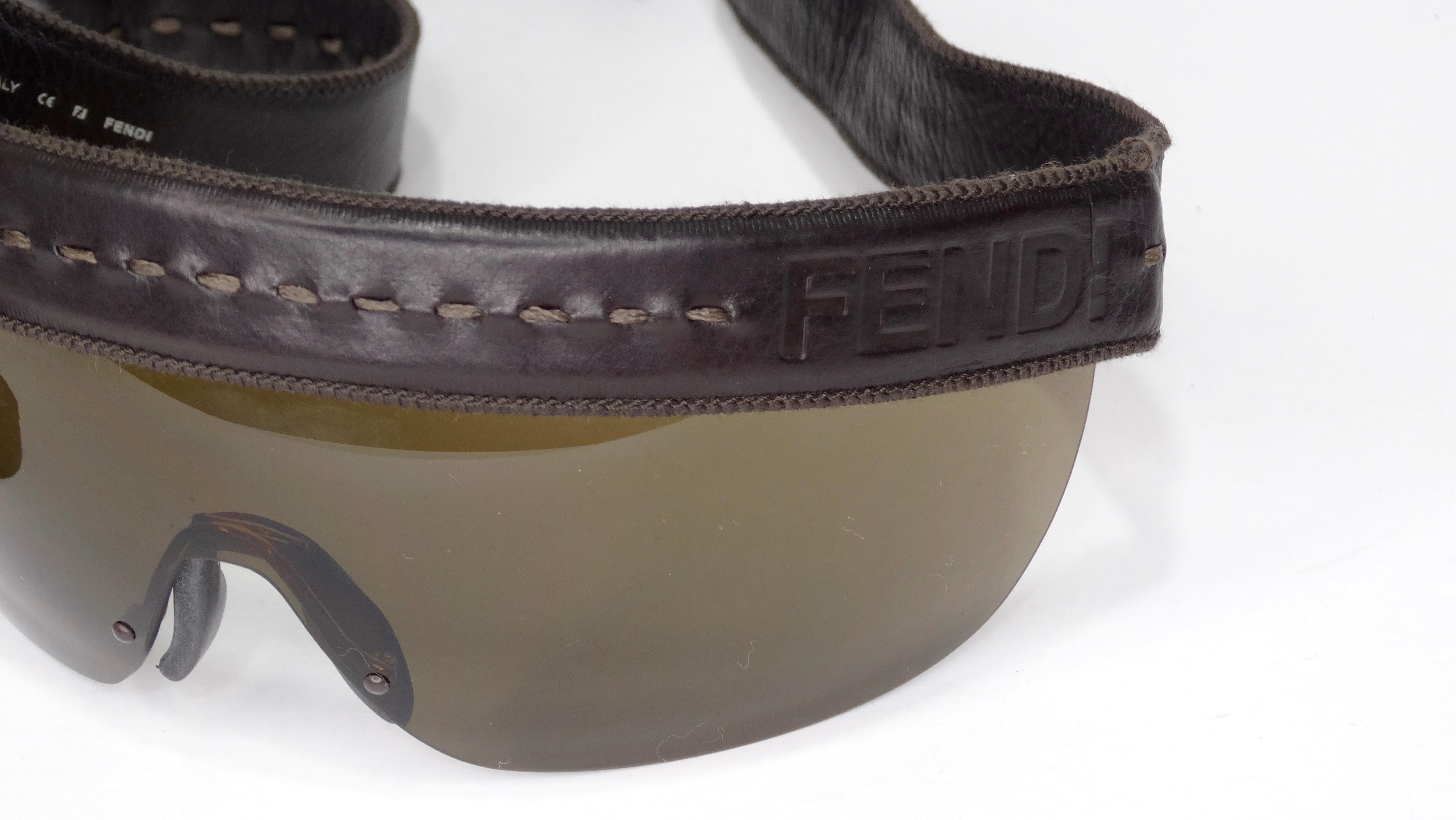 Elevate your look with these Fendi sunnies! Circa 1990s, these sunglasses feature a shield frame, dark brown lenses and a brown leather trim with fringe. Adjustable snap button closure head strap. Timeless and killer, these sunglasses are sure to be